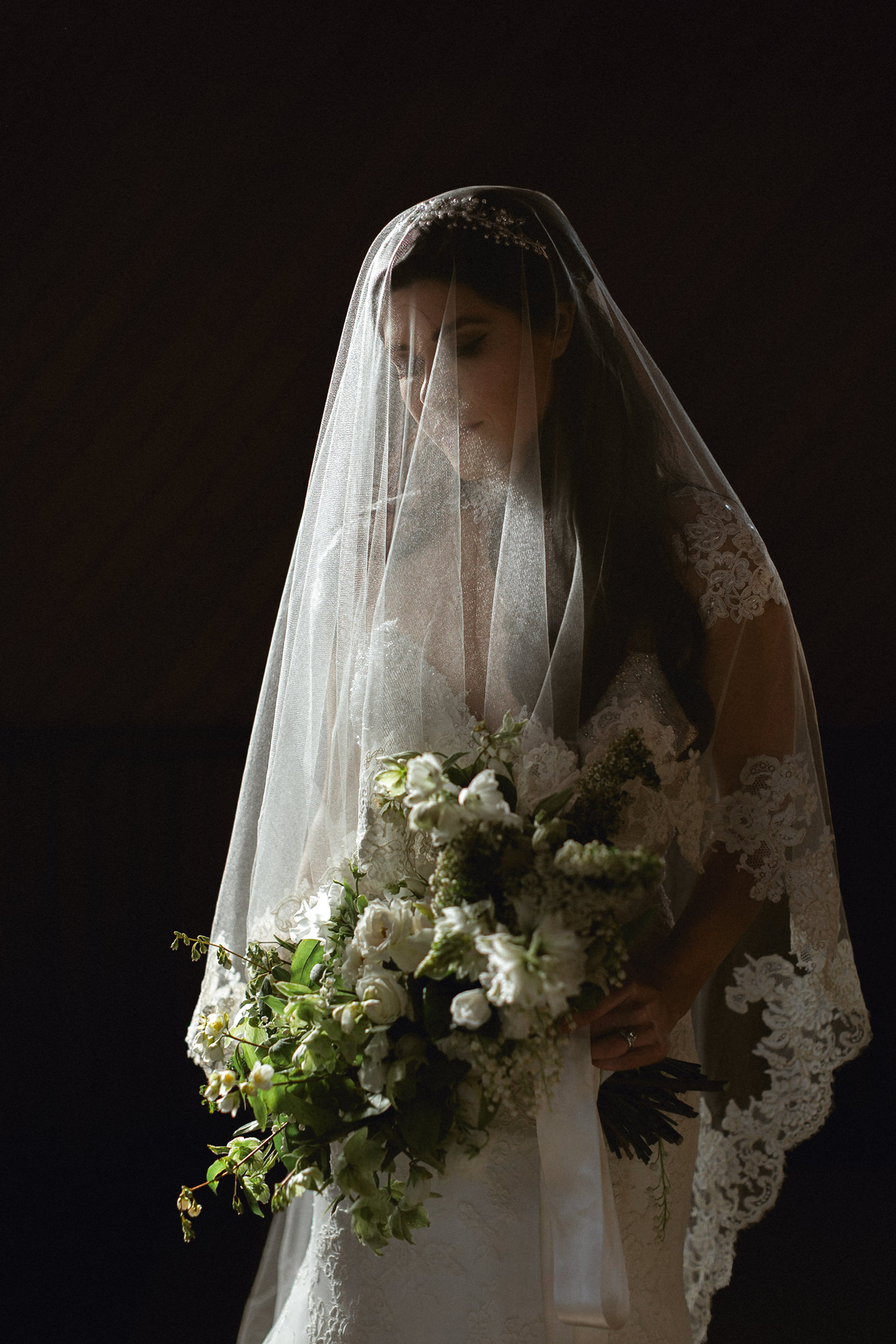 Bride in lace veil and white gown, holding large white and green bouquet, looks down calmly on her San Francisco wedding day.