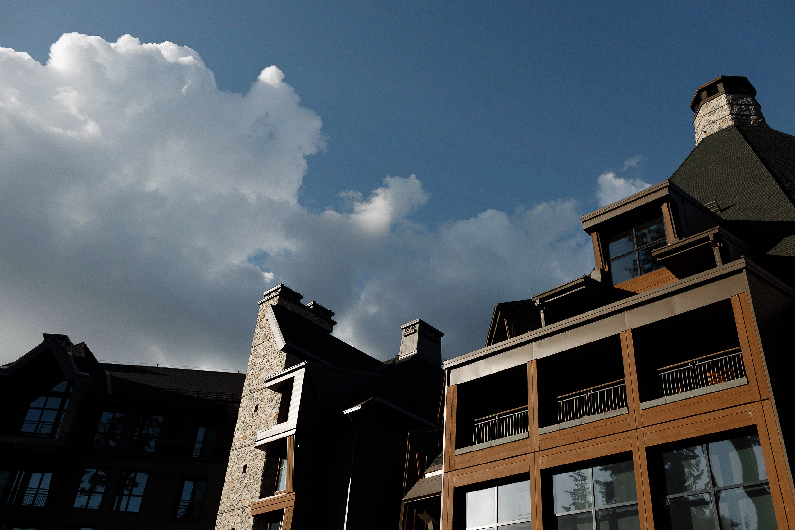 Modern wooden and stone buildings with balconies at The Ritz-Carlton, Tahoe, under a cloudy sky. Low angle highlights architecture.