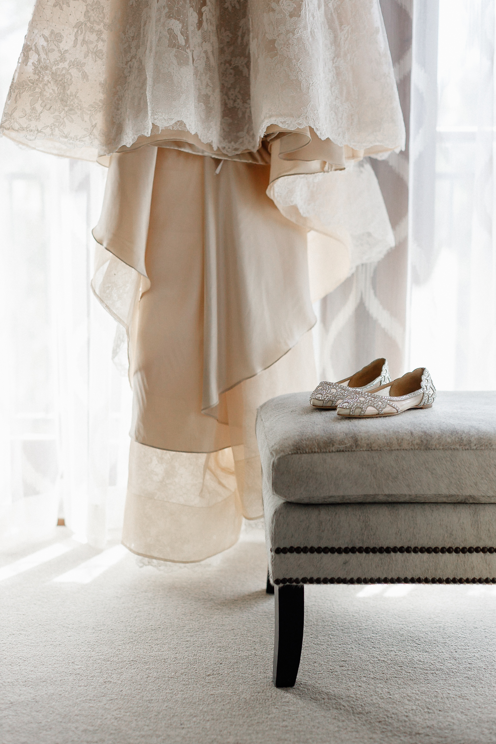 Close-up of a lace wedding dress and embellished shoes on a gray bench by a sunlit window at the Ritz-Carlton Lake Tahoe.