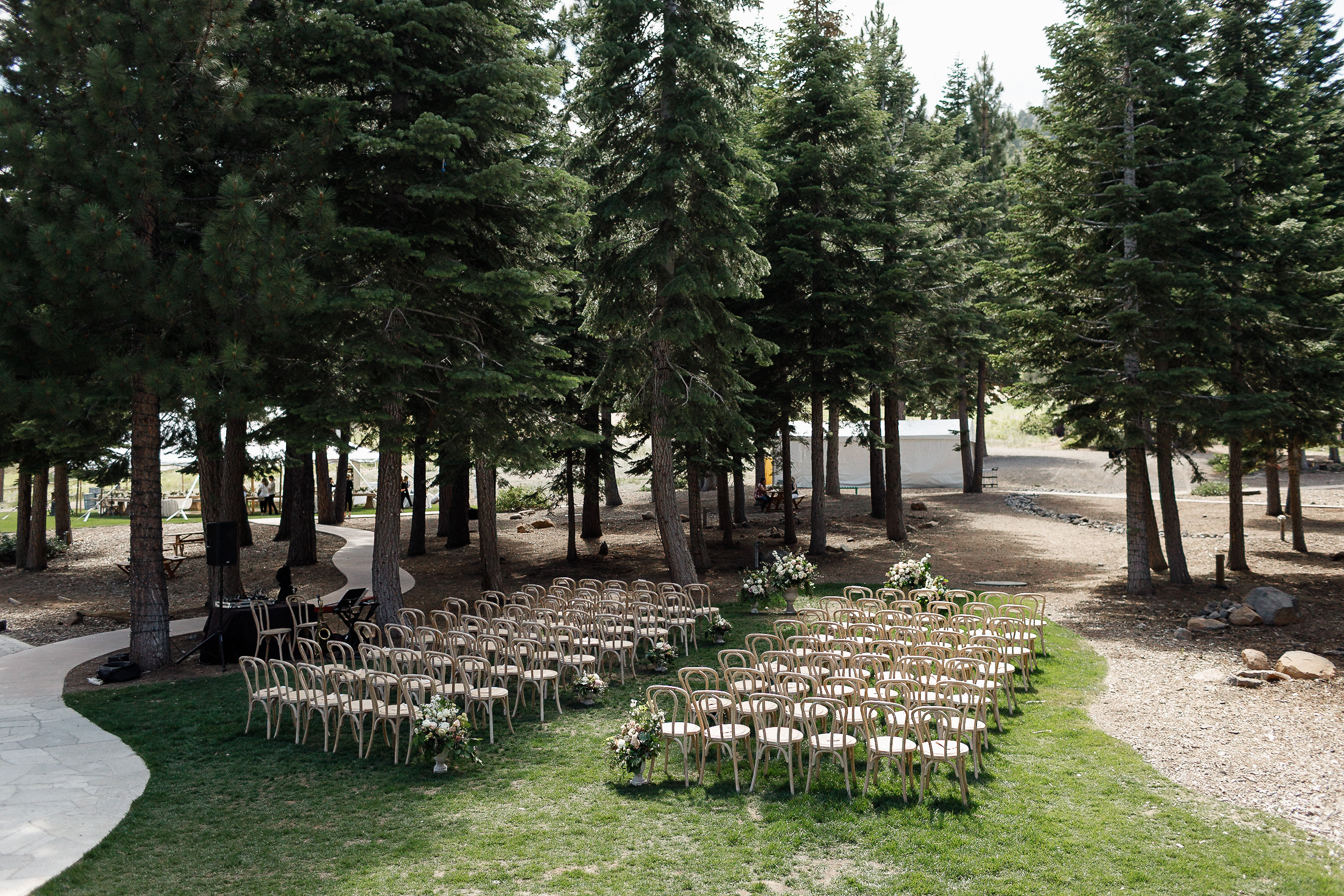 Chairs set up for a Ritz-Carlton wedding on grass by Lake Tahoe, with pine trees, aisle flowers, and sunlight through the branches.