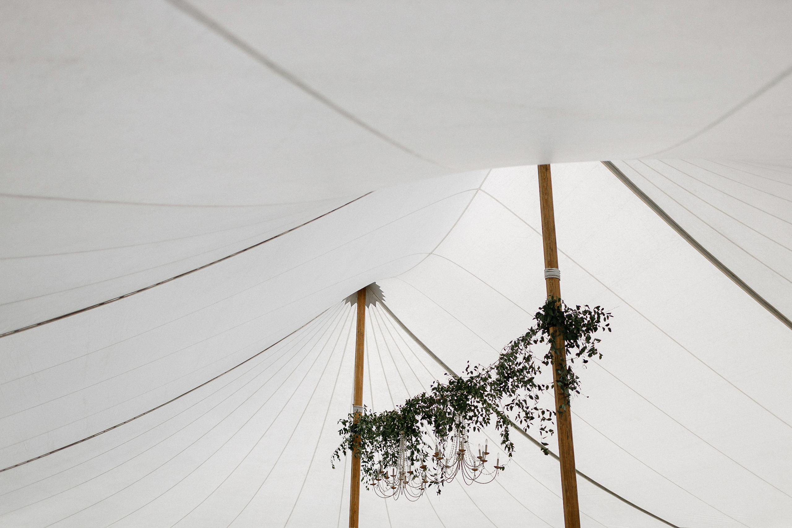 White tent ceiling with wooden poles, greenery draping, and central chandelier at Ritz-Carlton Lake Tahoe wedding.