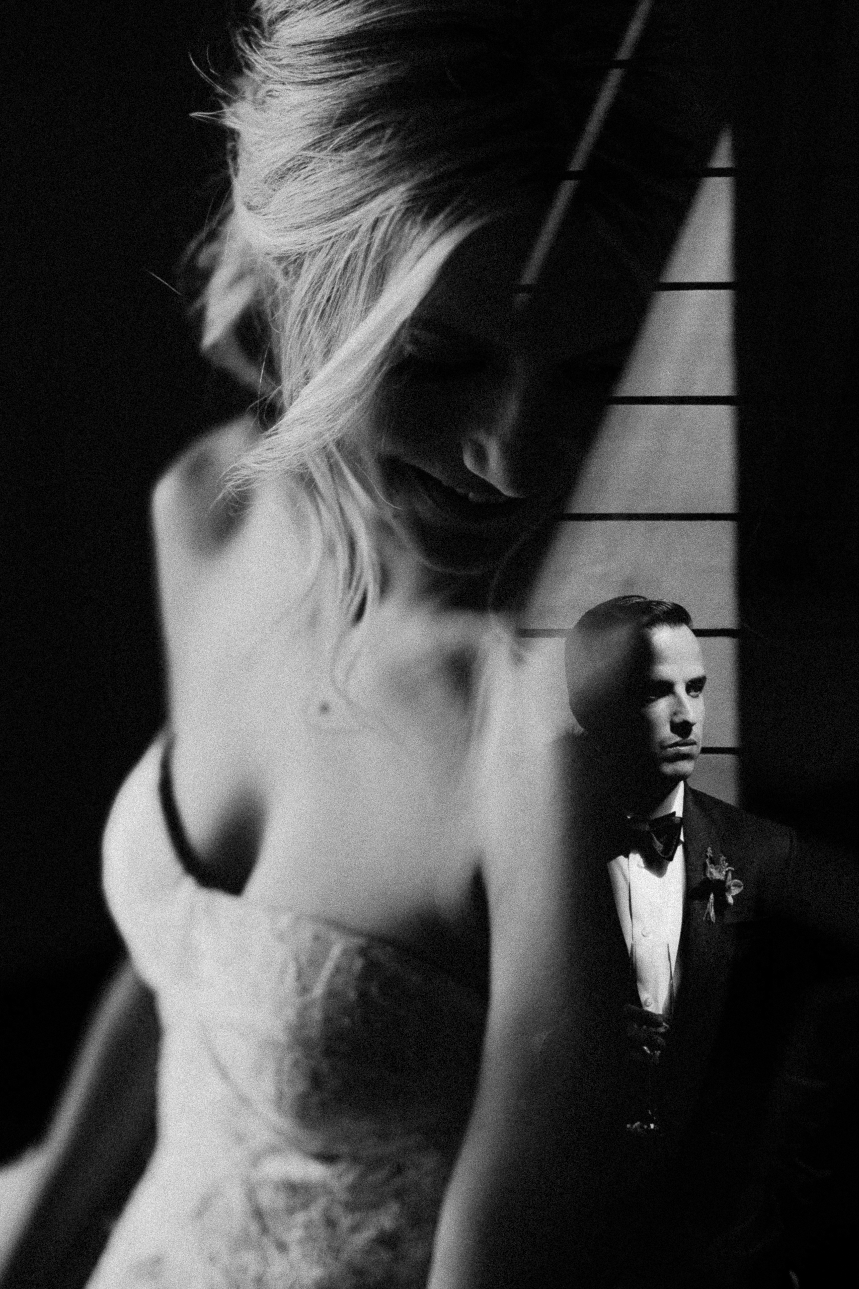 Black and white photo of a smiling bride, overlaid with a thoughtful groom in a suit, set against a dramatic shadowed background.