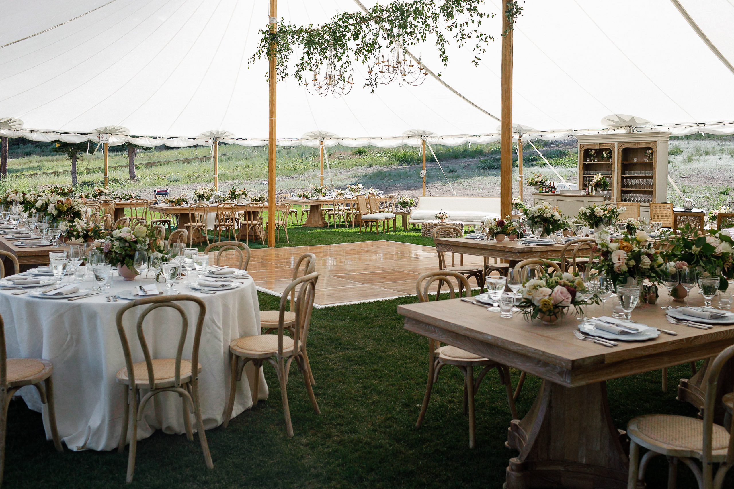 Outdoor wedding at Lake Tahoe under white tent with wooden and round tables, floral centerpieces, chandeliers, planned by Elise Events.