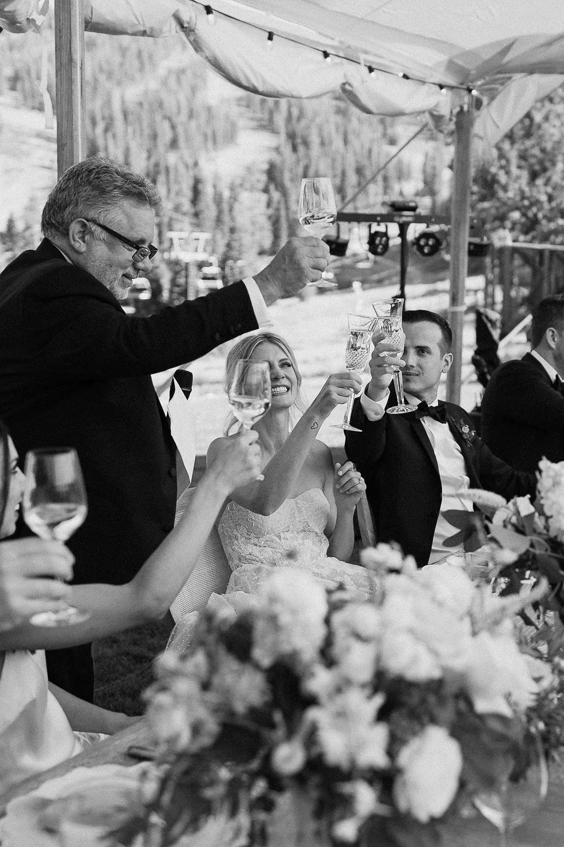 Well-dressed people at a decorated outdoor table at the Ritz-Carlton, Lake Tahoe, toast together with trees and mountains behind.