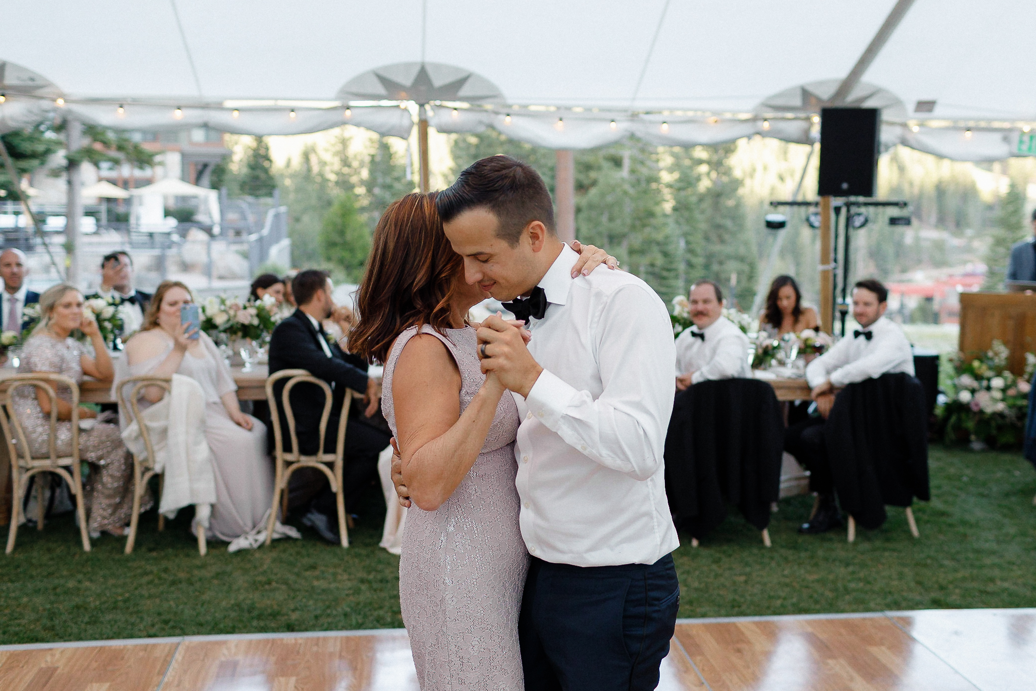 A man in a white shirt and bow tie dances with the bride in a light purple dress at a Lake Tahoe wedding under a decorated tent.
