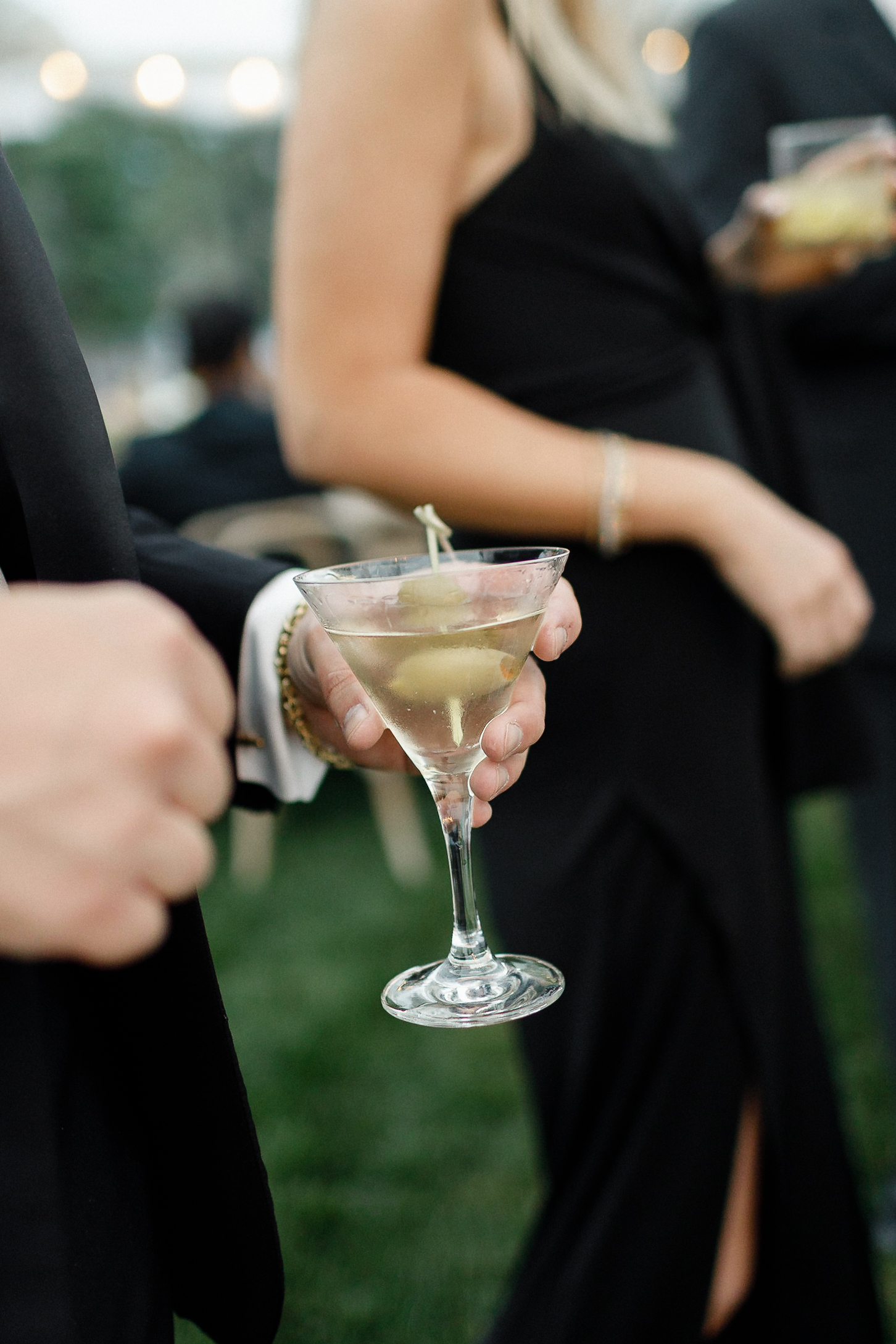 A person in formal attire holds a martini with an olive beside another guest in black at an outdoor Lake Tahoe event.