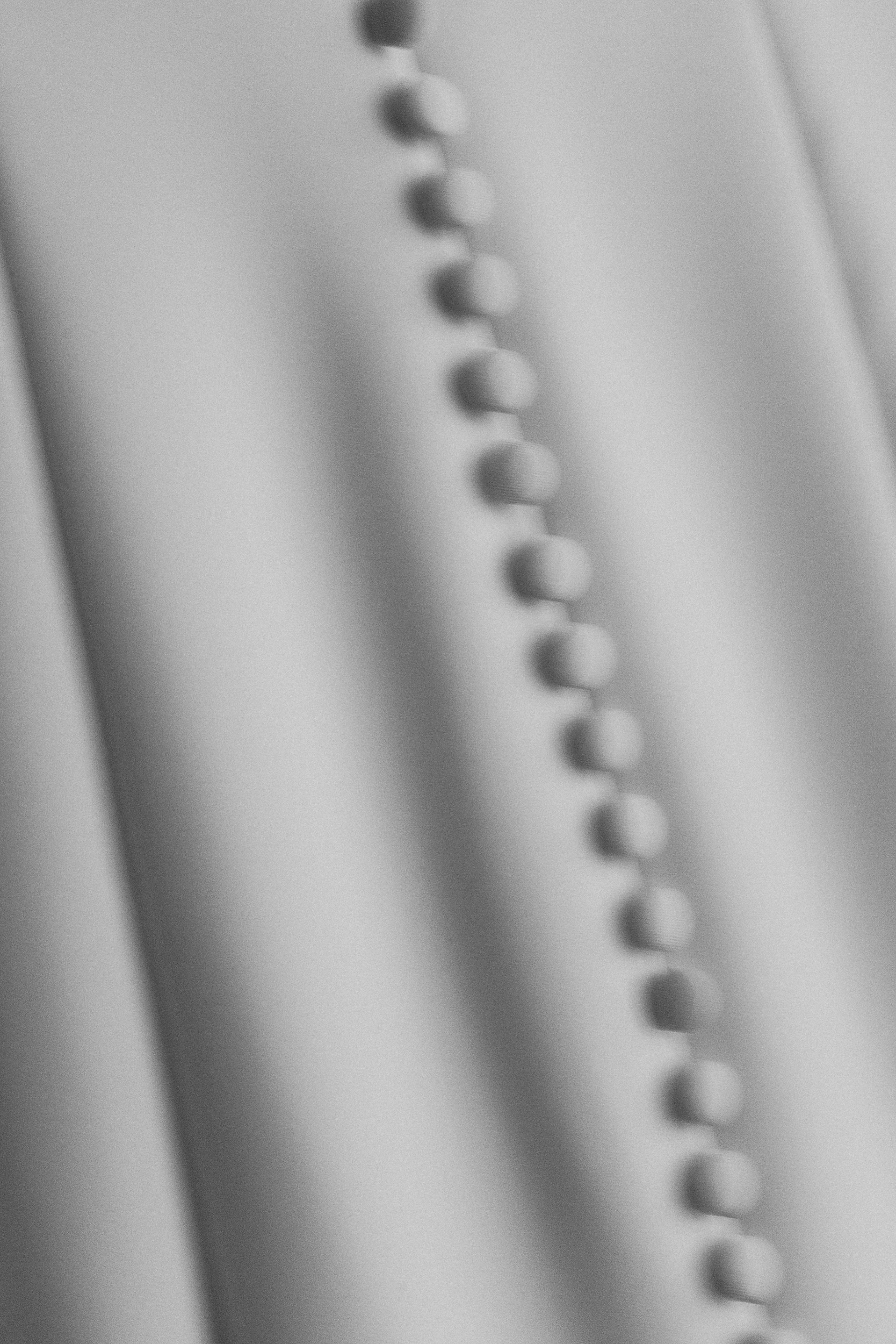 Close-up of round buttons on smooth, light fabric, likely a bridal gown; soft, blurred focus gives the image a gentle look.