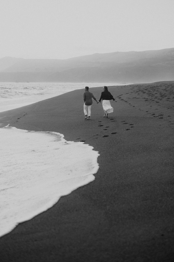Black & white engagement photo of couple on a San Francisco beach; timeless romance in every frame.