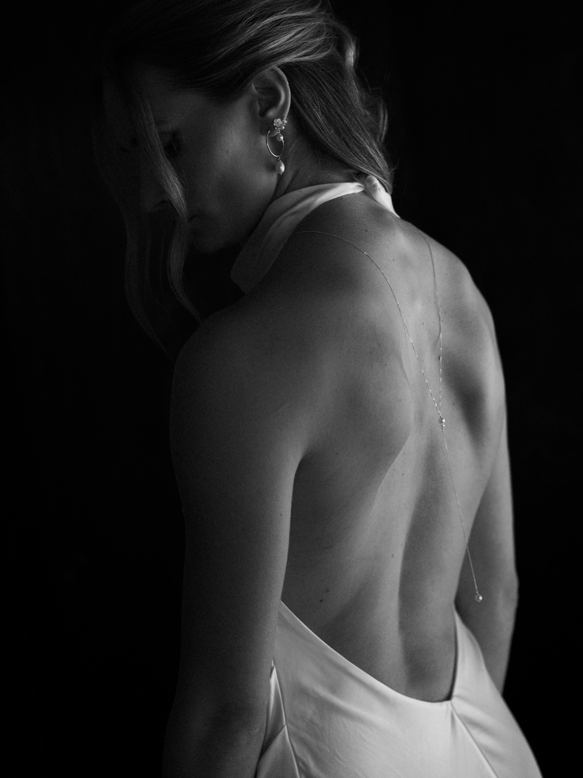 Woman in a backless dress, facing away, with soft lighting on her back. Black and white photo set in San Francisco; simple jewelry.