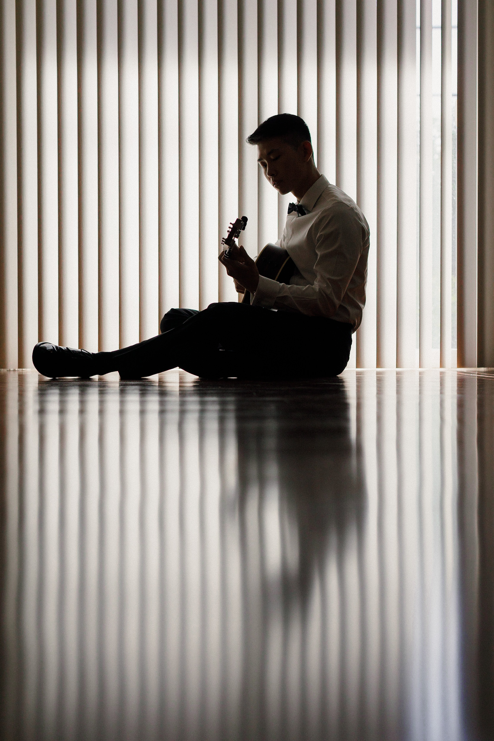 Elegant silhouette of a graduate in formal attire, strumming an acoustic guitar in soft lighting.