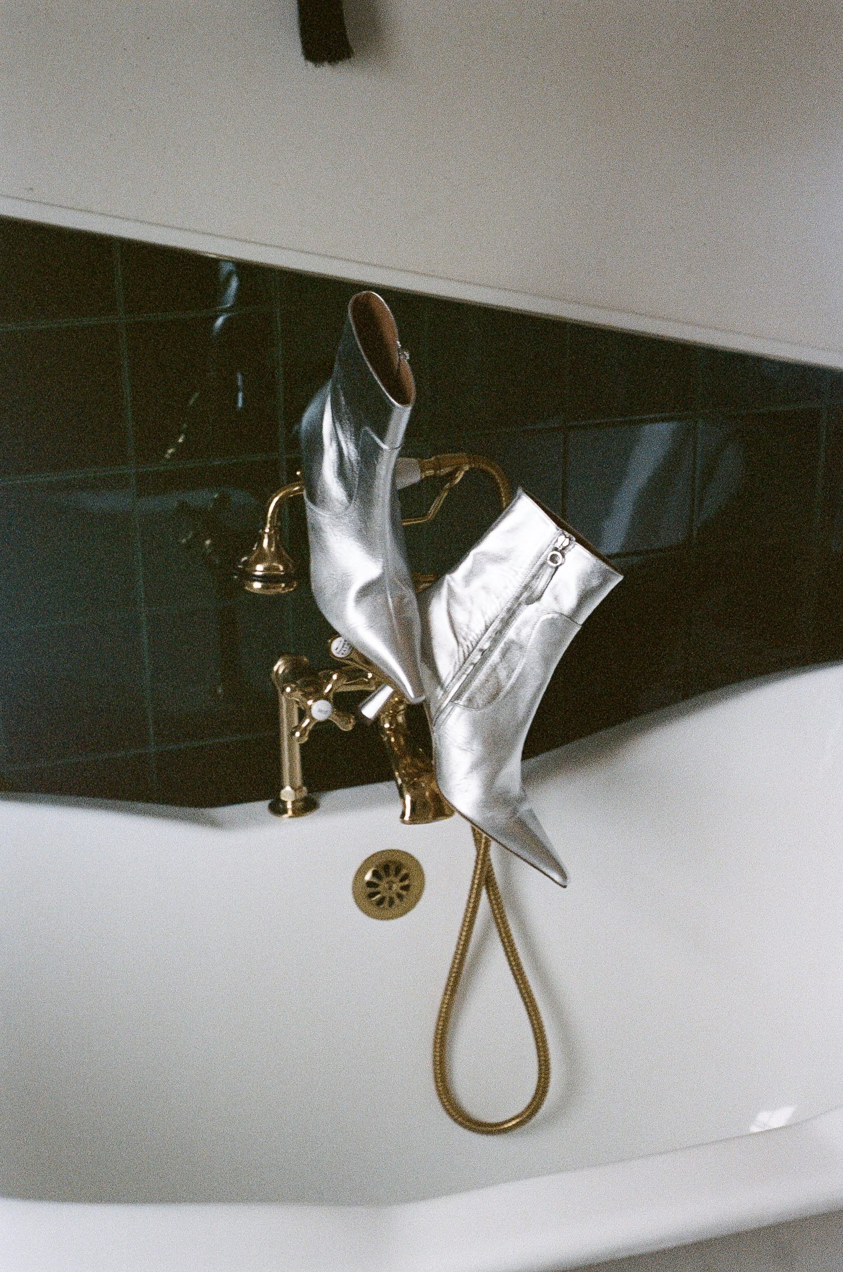 Silver high heels elegantly draped on a gold faucet, contrasted with lush Mendocino green tiles.