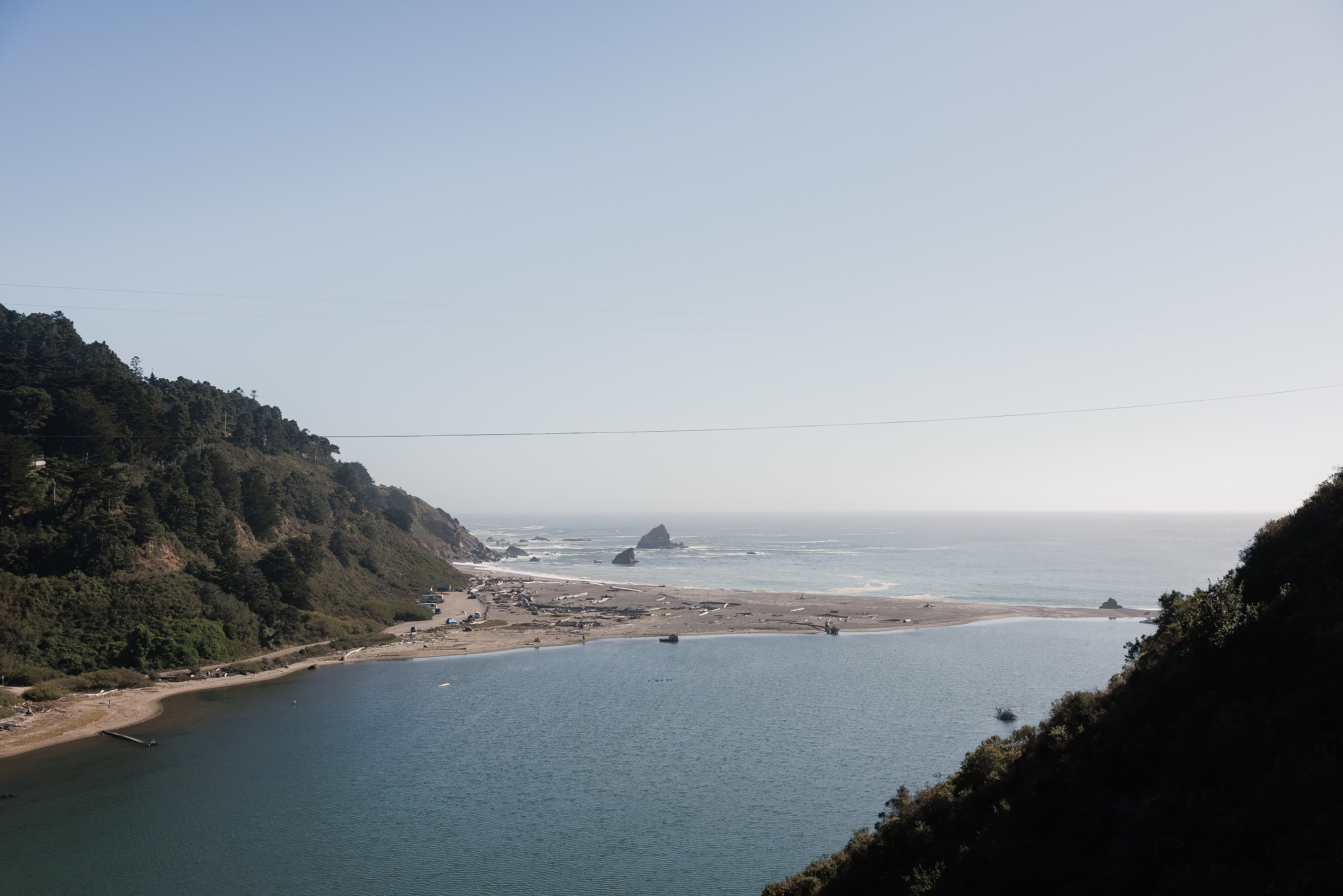 Capture the serene beauty of Mendocinos coast: where river meets ocean amidst rocky cliffs and lush greenery.
