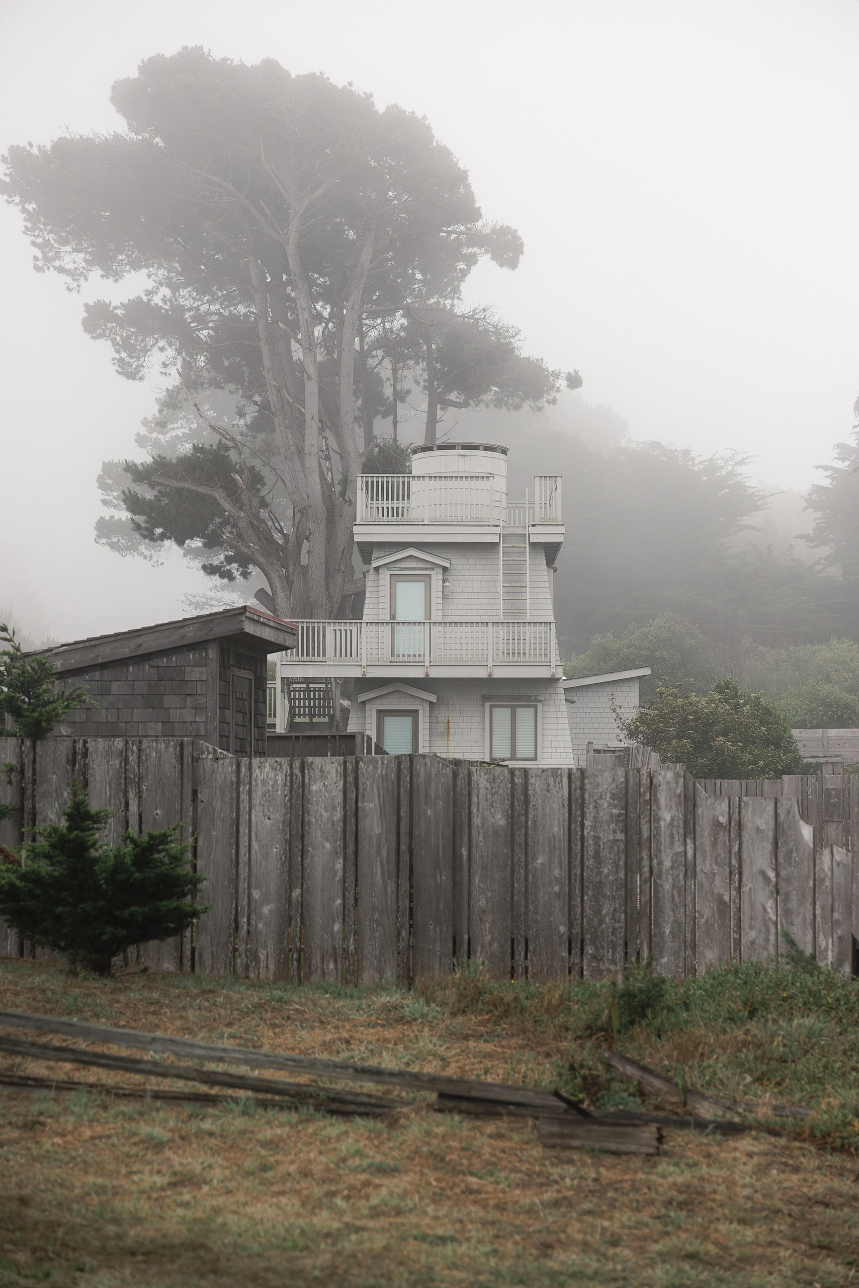 Elegant white mansion with balconies, misty Mendocino backdrop. Captivating wedding venue photography.