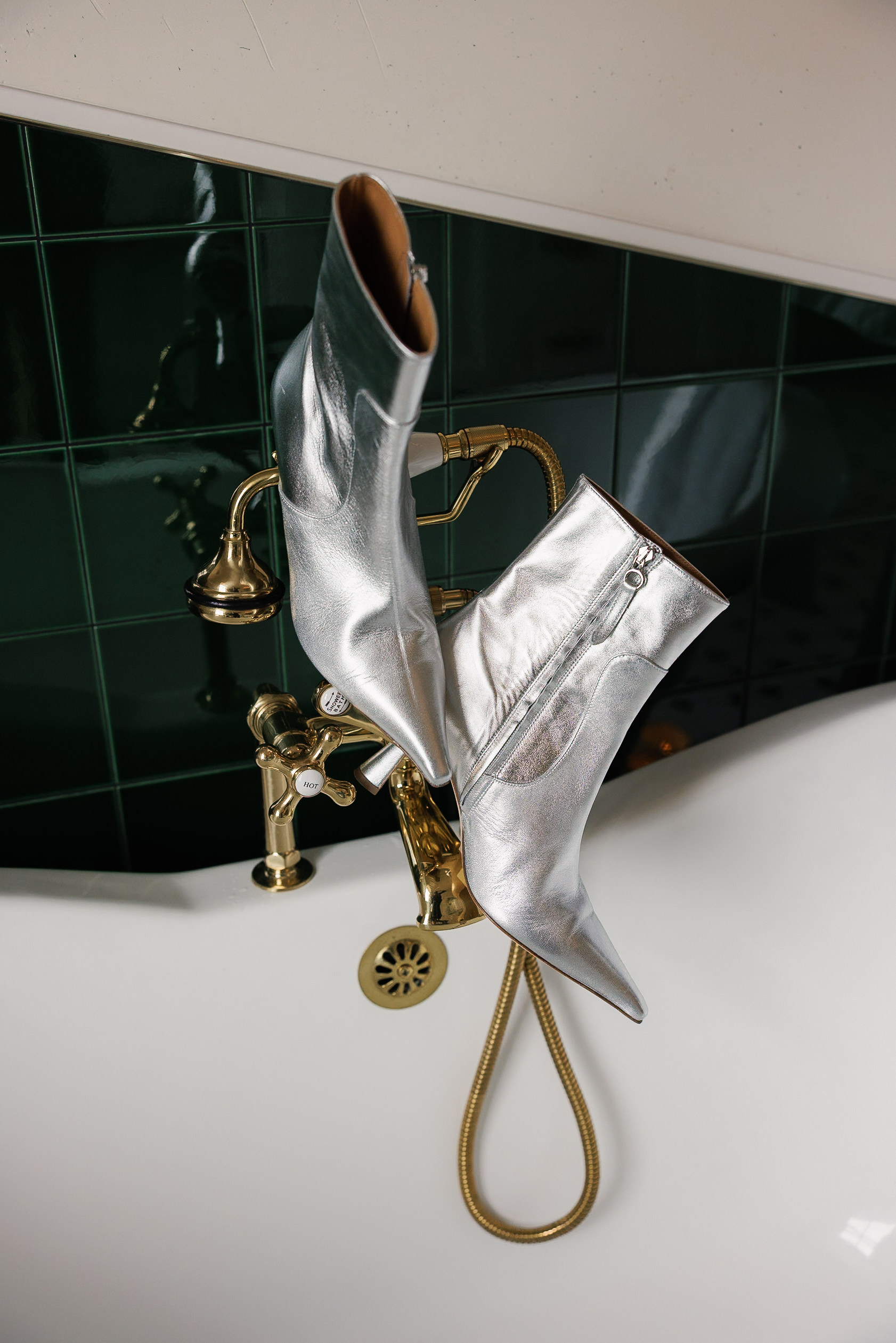 Silver high-heeled boots on gold faucet in luxurious Mendocino; dark green tiles add elegance.