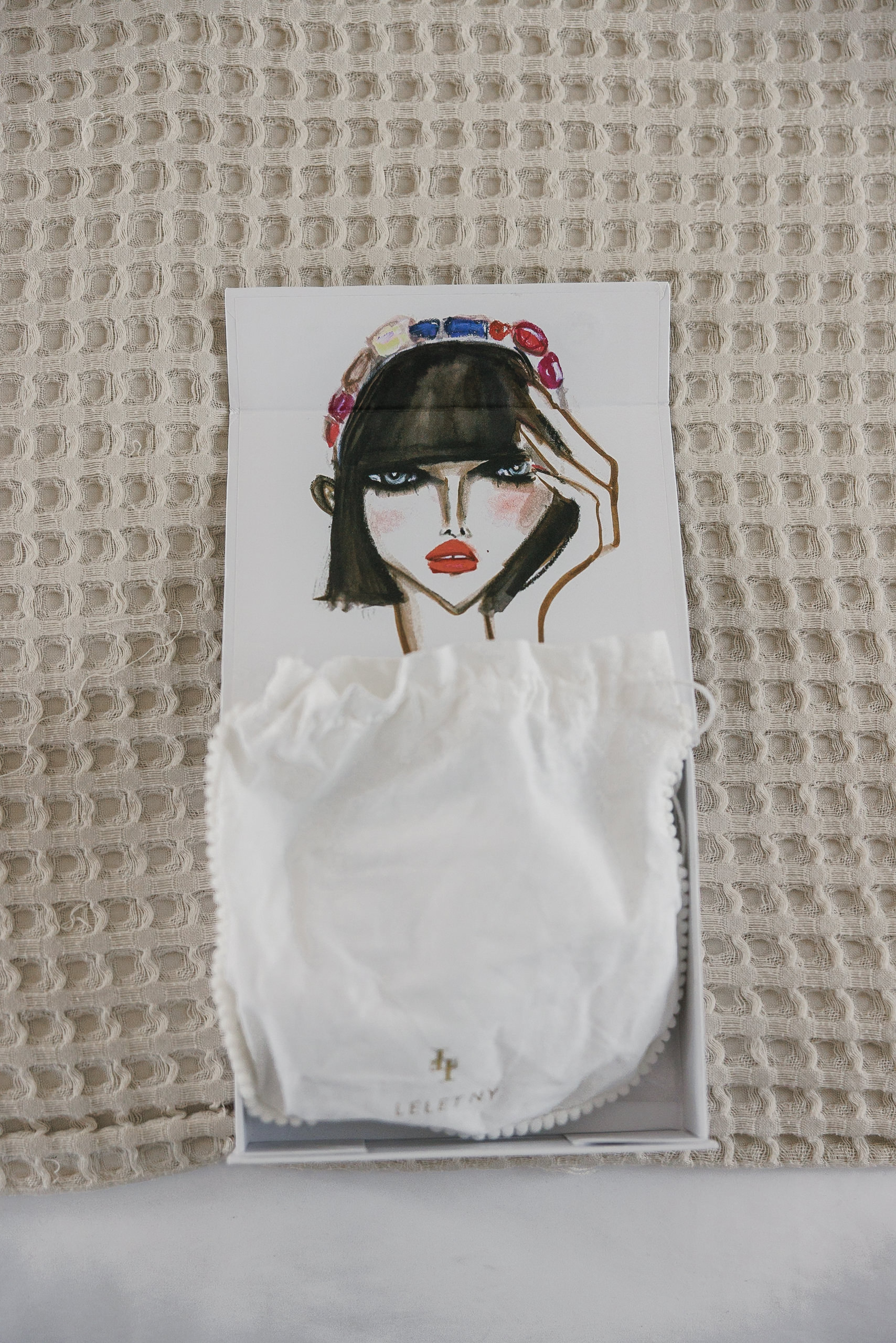 Capture elegance: A Mendocino box revealing a vibrant illustration and chic white accessory on textured backdrop.