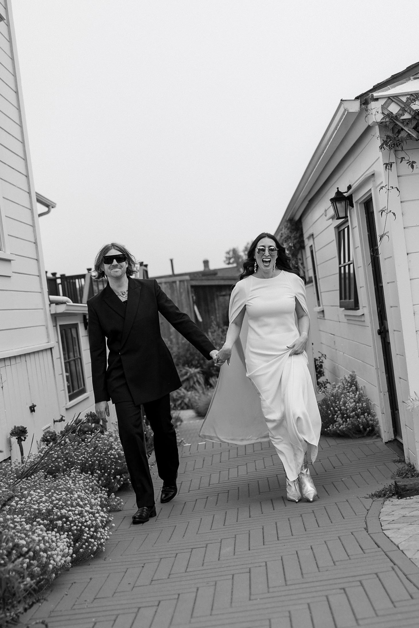 Black & white photo: Joyful couple walking hand in hand on a scenic Mendocino path.