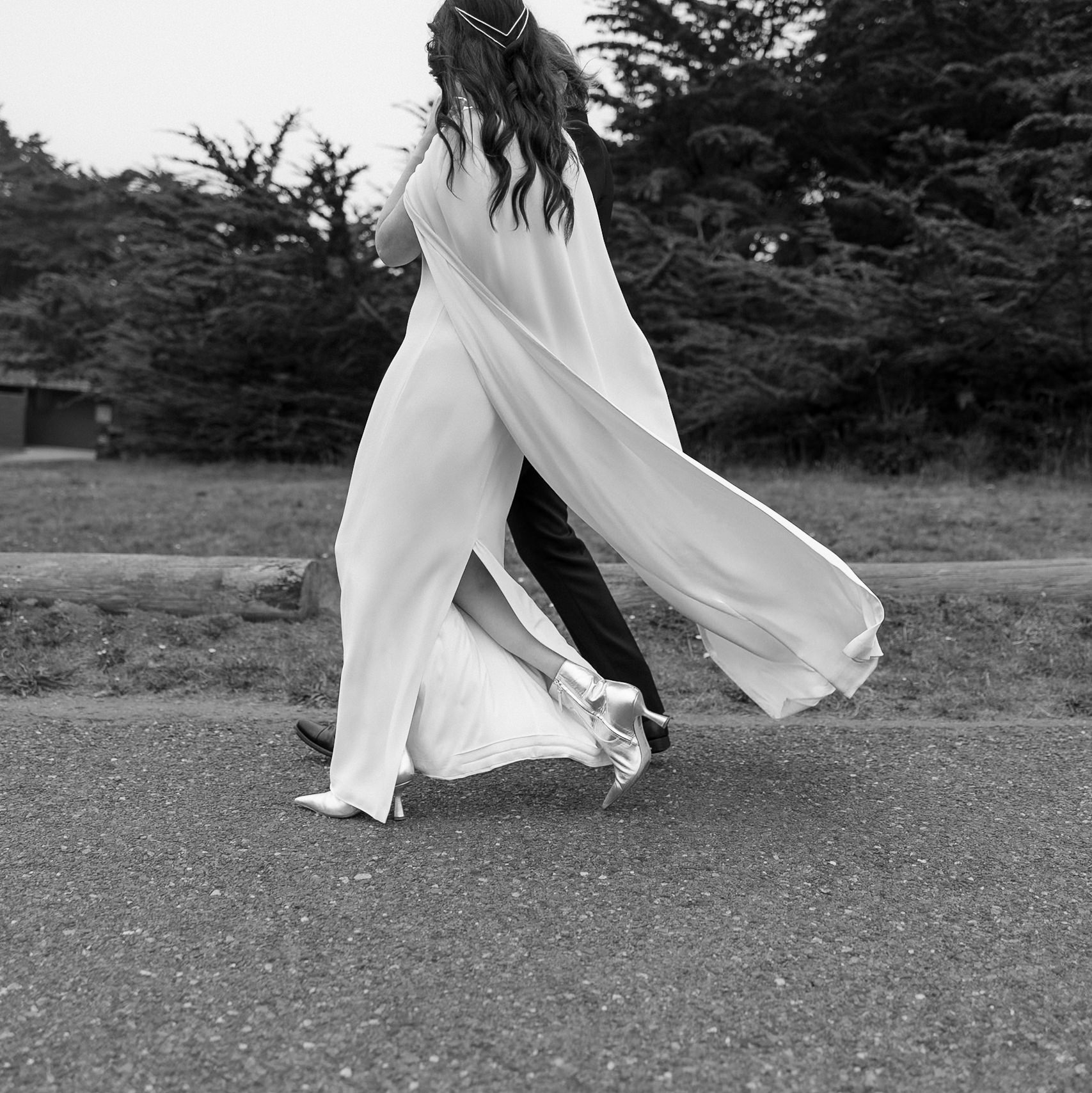 Elegant bride in Mendocino: flowing white dress, silver heels; graceful path, black and white photography.