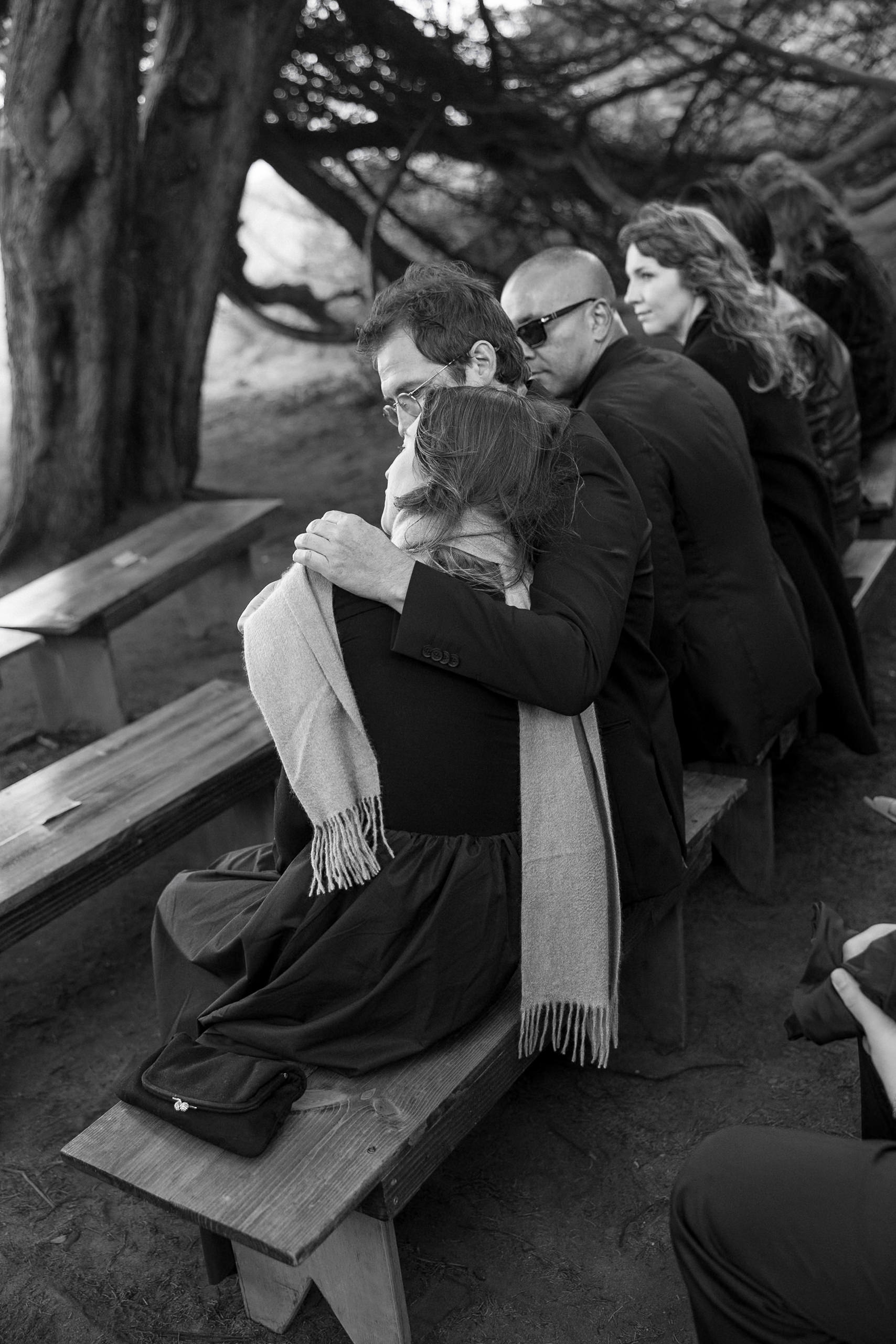 Elegant Black & White Wedding Photography in Mendocino: Couple Embrace Among Forested Benches.