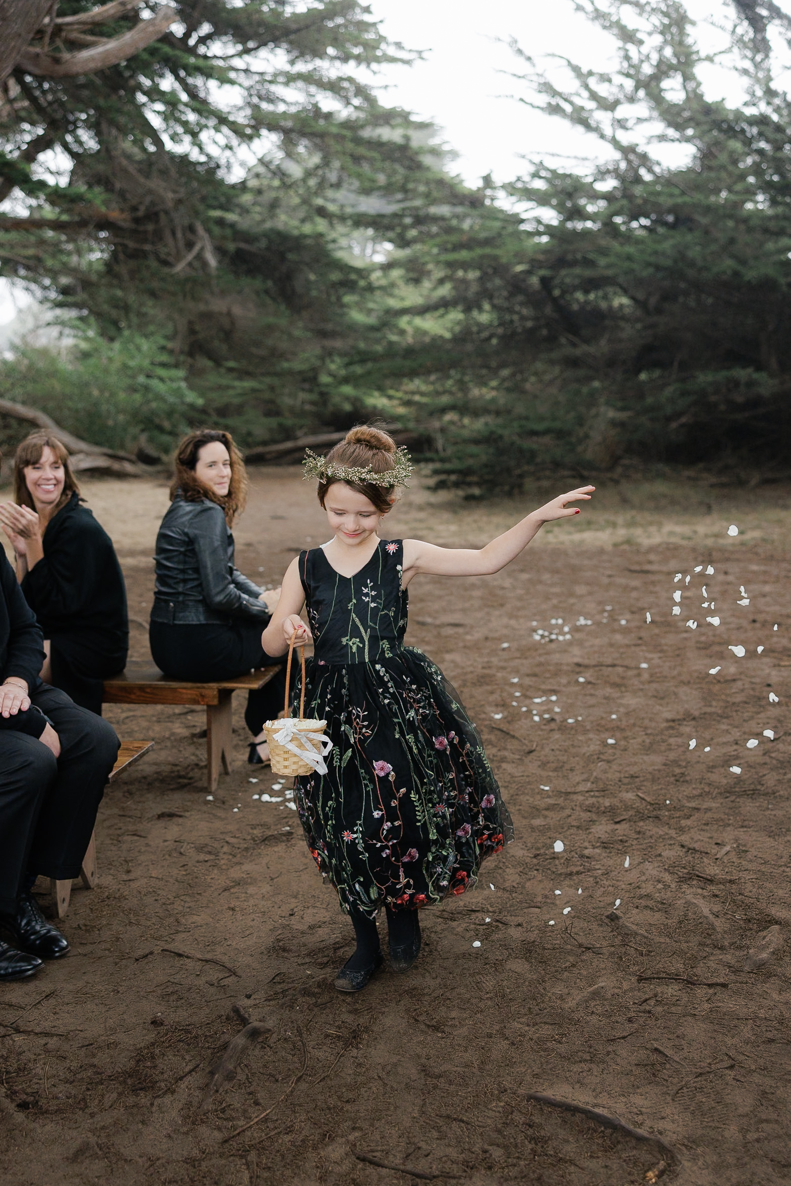 Capture the essence of Mendocino weddings: A girl in a floral dress scatters rose petals under lush trees.