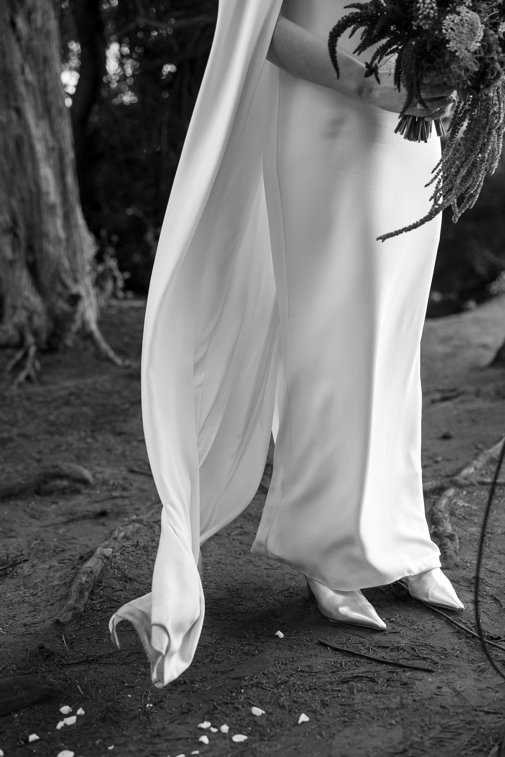 Black & white Mendocino wedding photo: flowing dress, bouquet, shoes on a dirt path amidst trees.