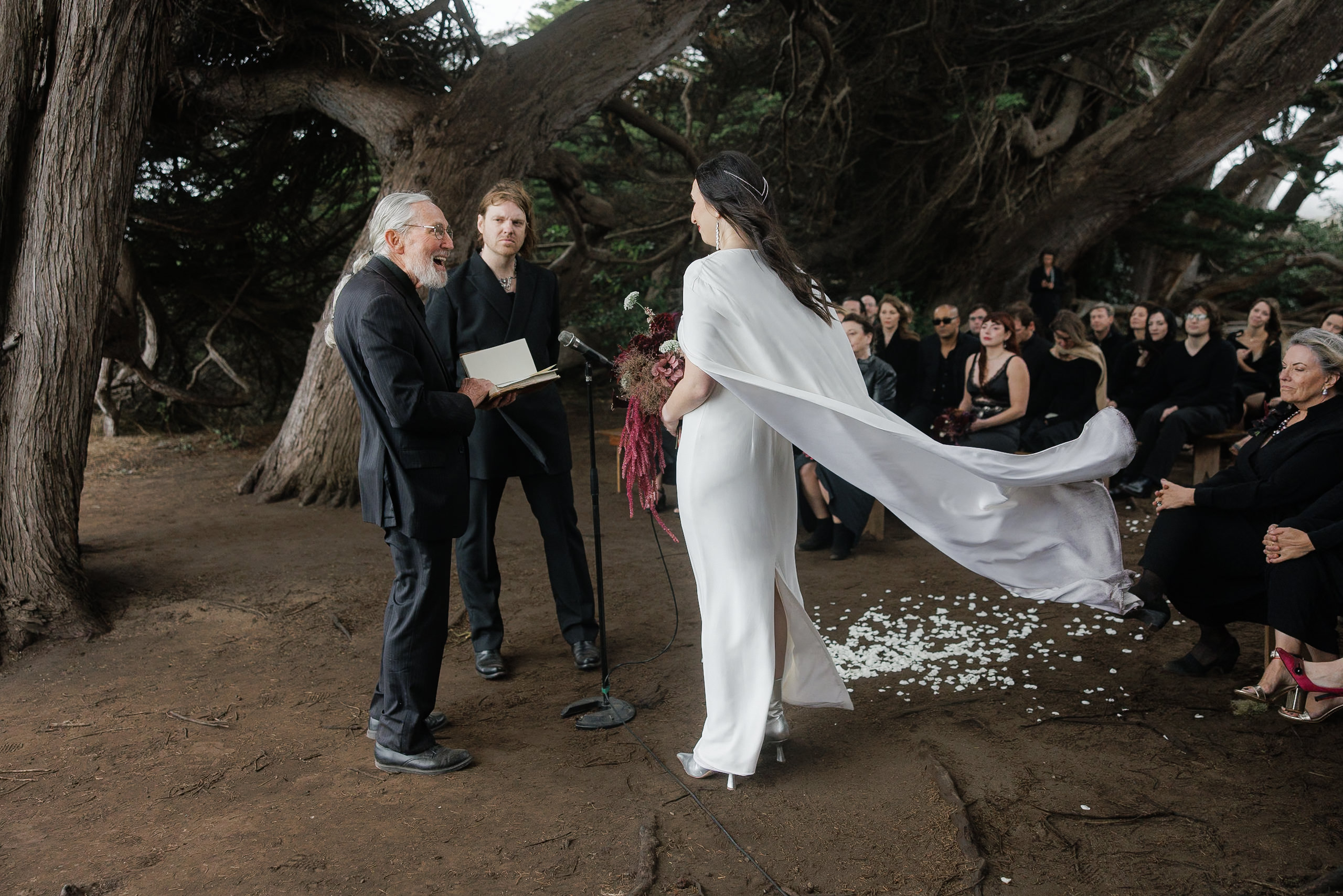 A bride in flowing white graces a tranquil outdoor ceremony beneath Mendocinos towering trees.