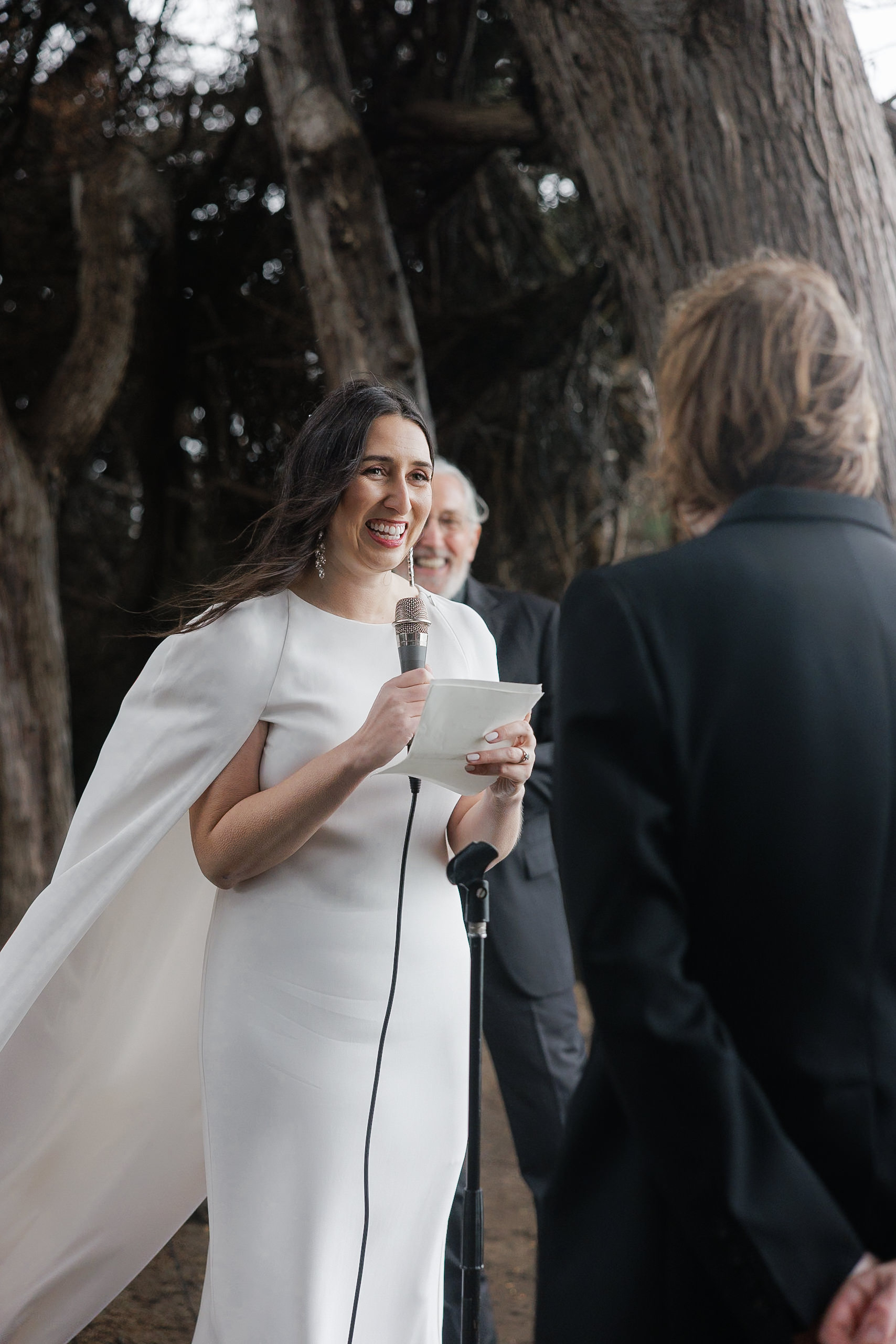 Captivating Mendocino Wedding Photography: Bride Joyously Speaks Amidst Majestic Forest Backdrop.