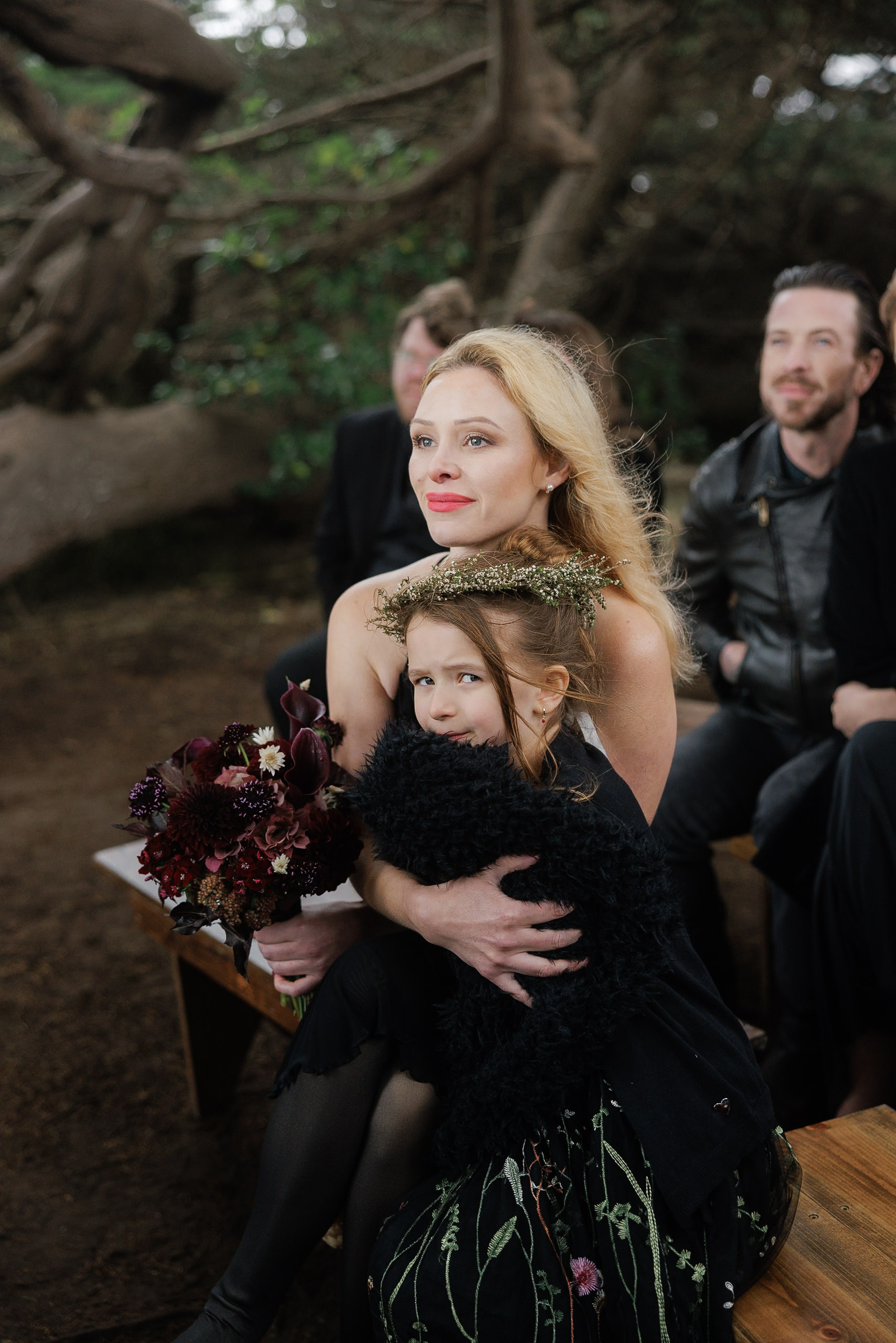 Capture intimate wedding moments in Mendocino: Blonde bride embraces girl in dark floral setting.