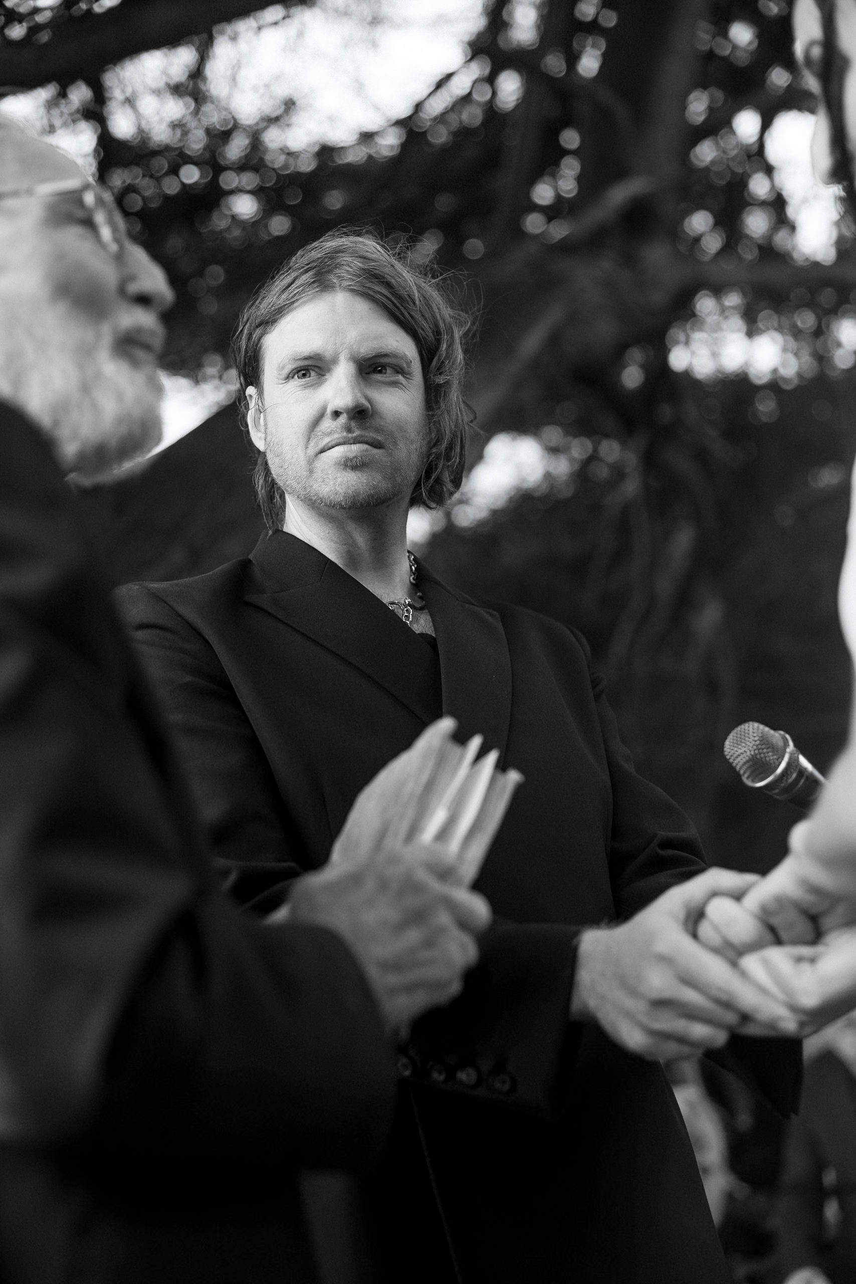 Elegant outdoor ceremony in Mendocino: Black & white portrait of speaker under grand trees.