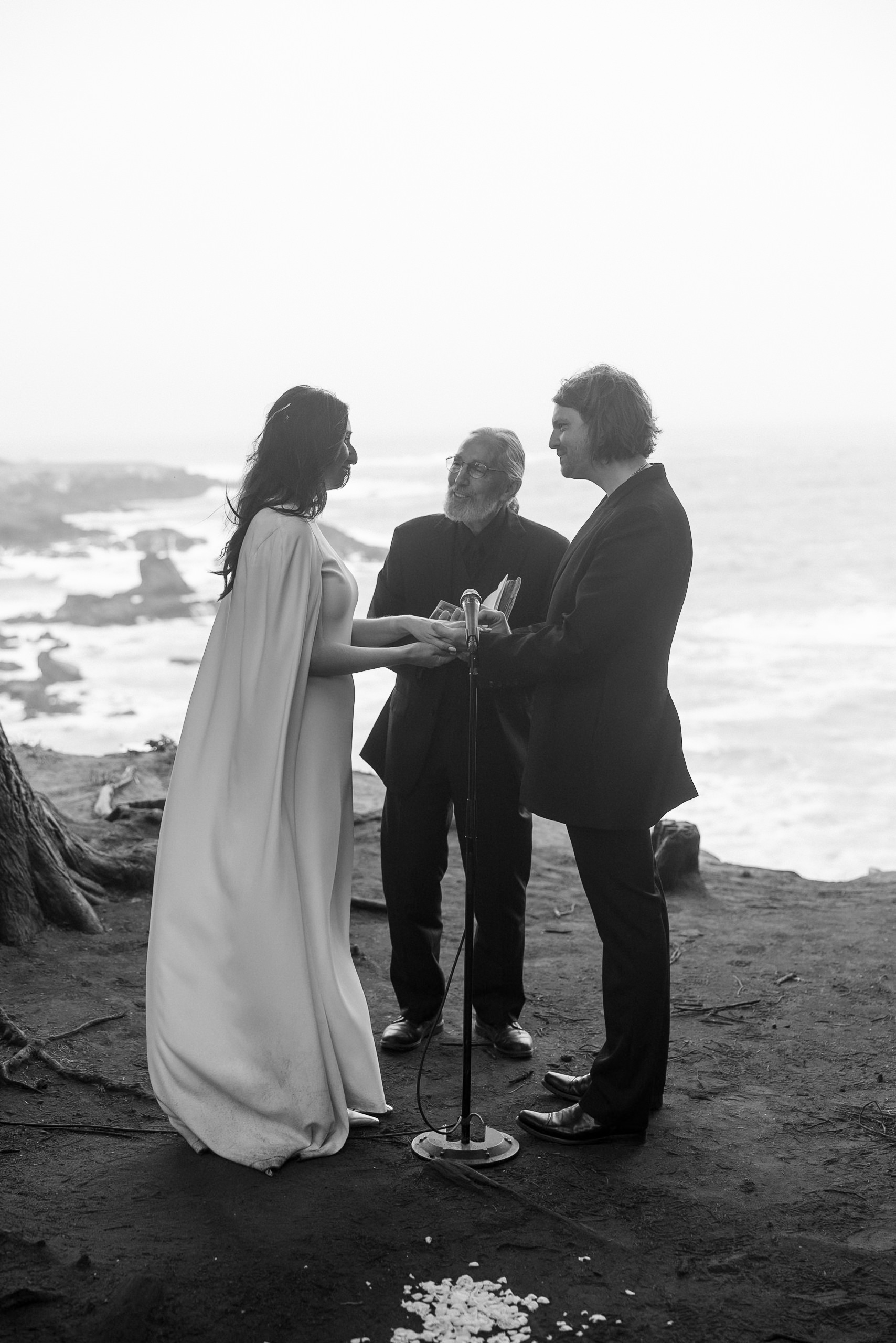 High-end Mendocino wedding on coastal cliff: couple holds hands, officiant presides, waves crash.