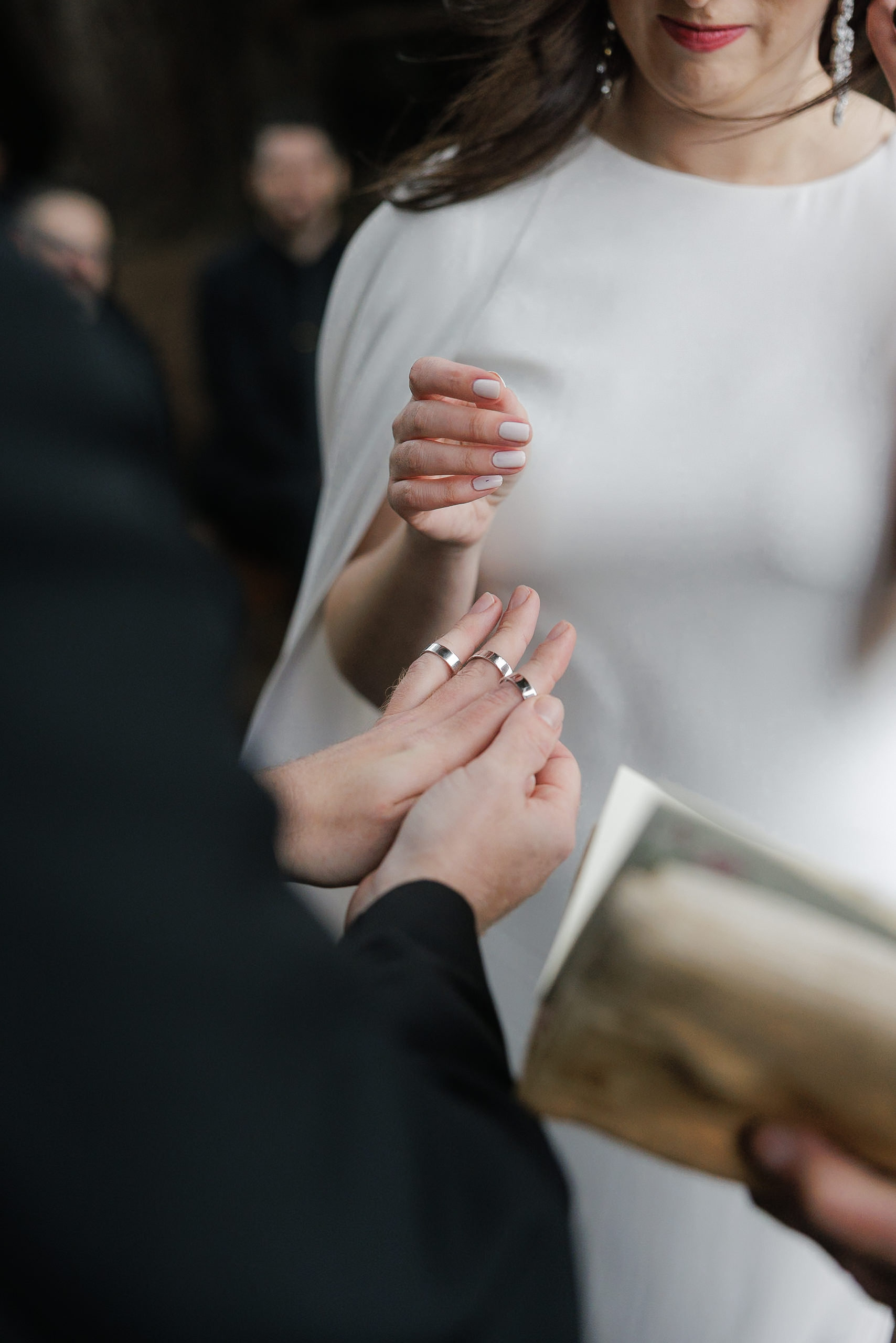 Close-up of Mendocino wedding ring exchange; bride in white dress, light pink nails.
