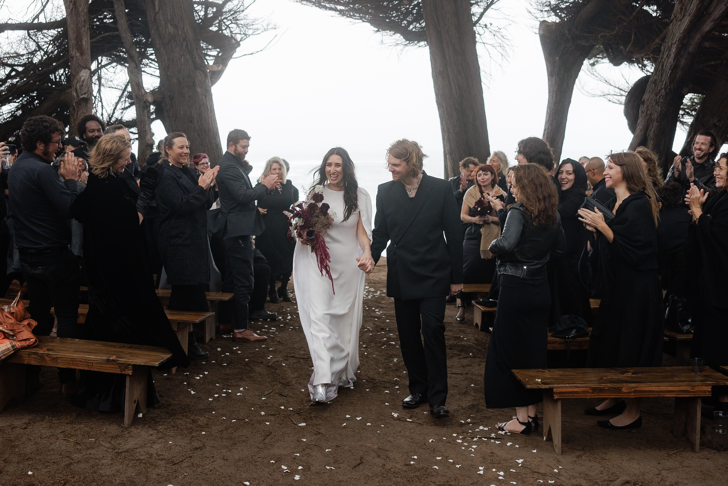 Elegant Mendocino Wedding: Bride in White with Bouquet, Groom in Black Suit, Outdoor Ceremony under Majestic Trees.