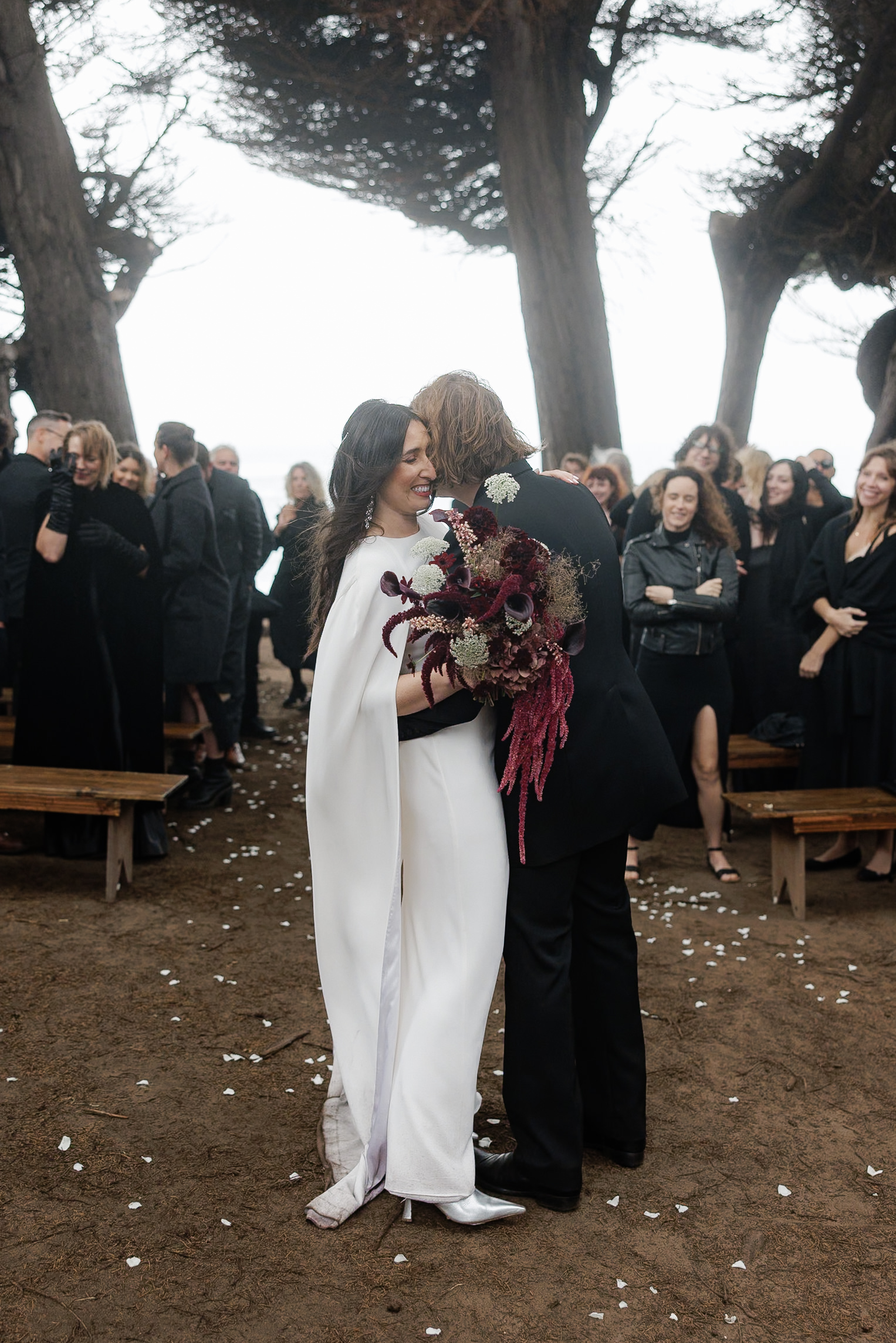 Elegant Wedding Photography in Mendocino: Bride & Grooms Outdoor Embrace Amid Guests.
