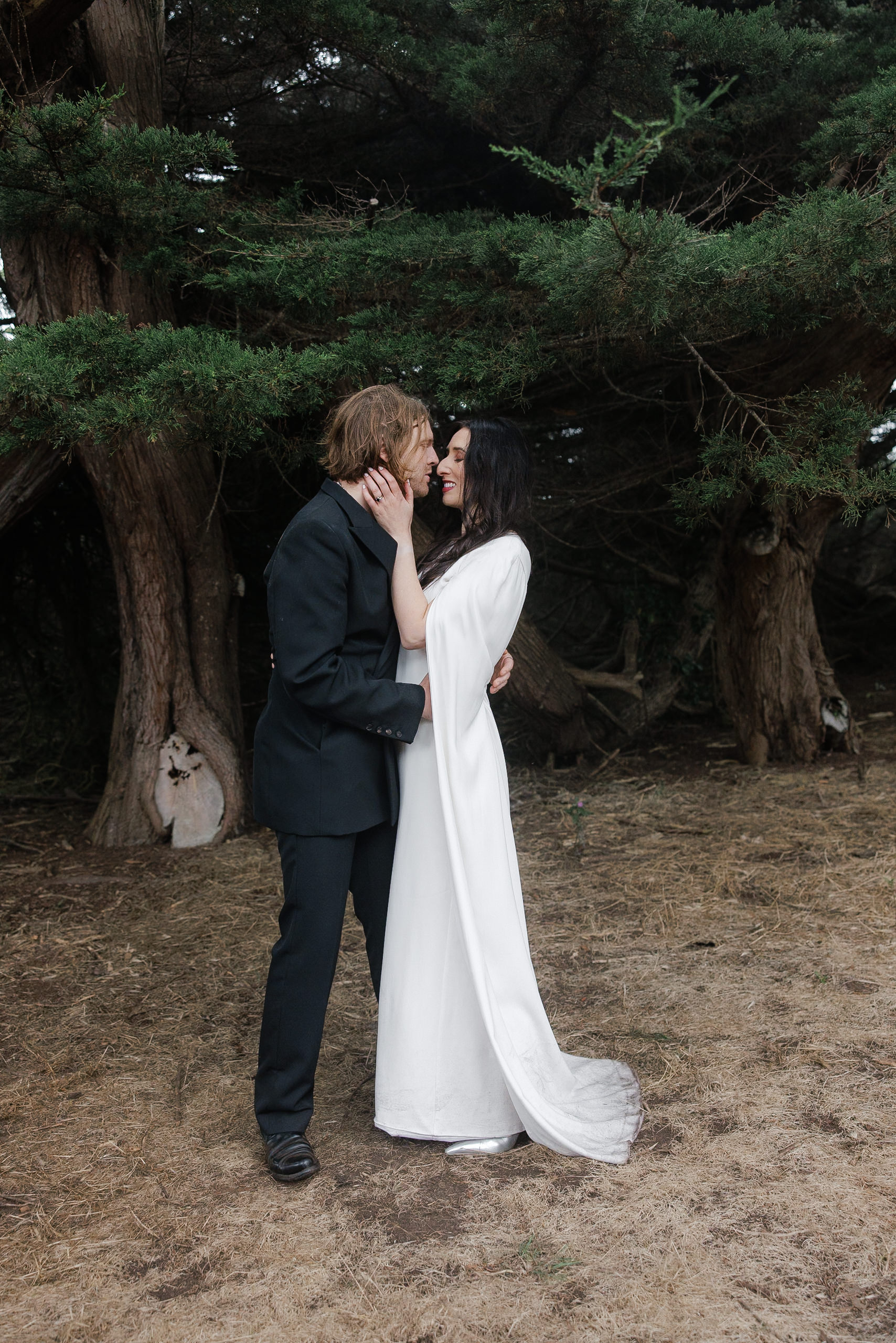 Enchanting Mendocino wedding: couple embraces amidst majestic trees, captured in serene elegance.