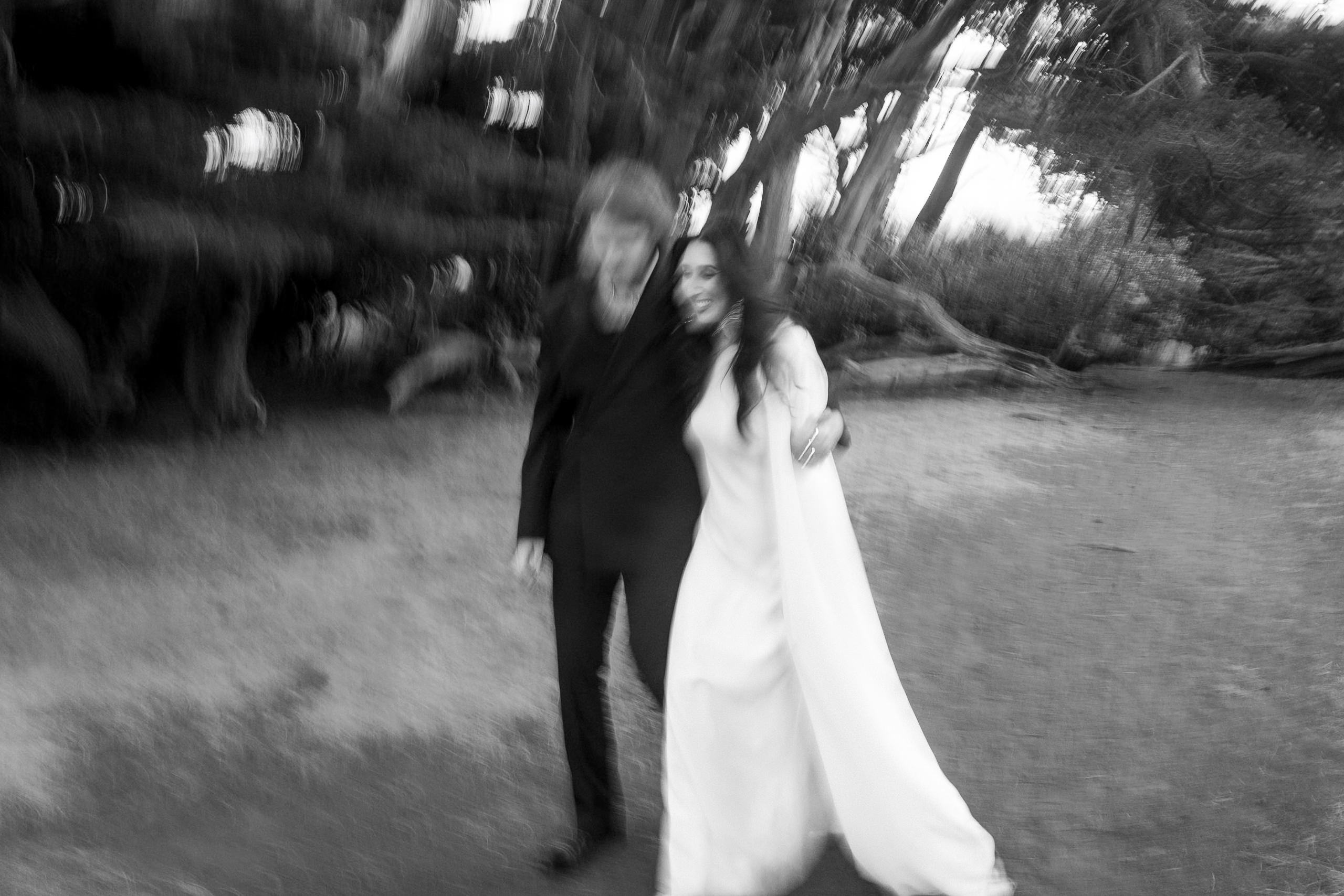 Black & White Wedding Photo: Couple Walks Arm in Arm Through Enchanting Mendocino Landscape.