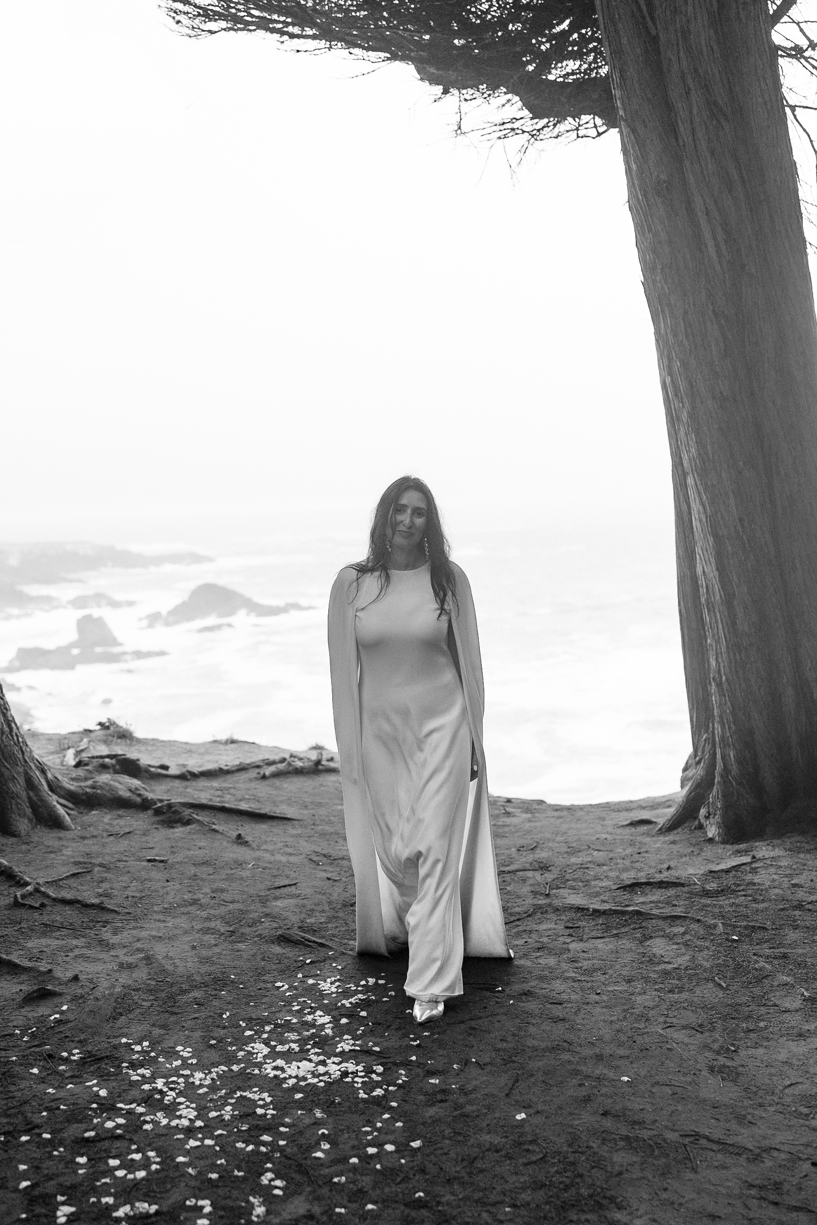 Elegant bride in flowing dress, Mendocino coast, windswept trees and crashing waves; timeless black & white.