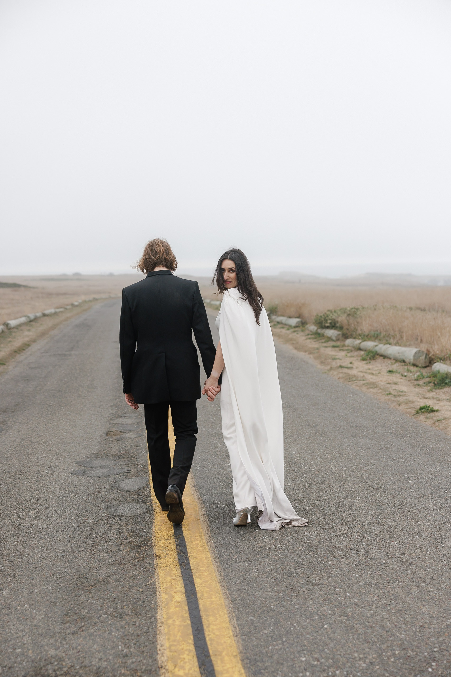 Elegant Wedding Photography in Mendocino: Couple Strolls Through Scenic Landscape.
