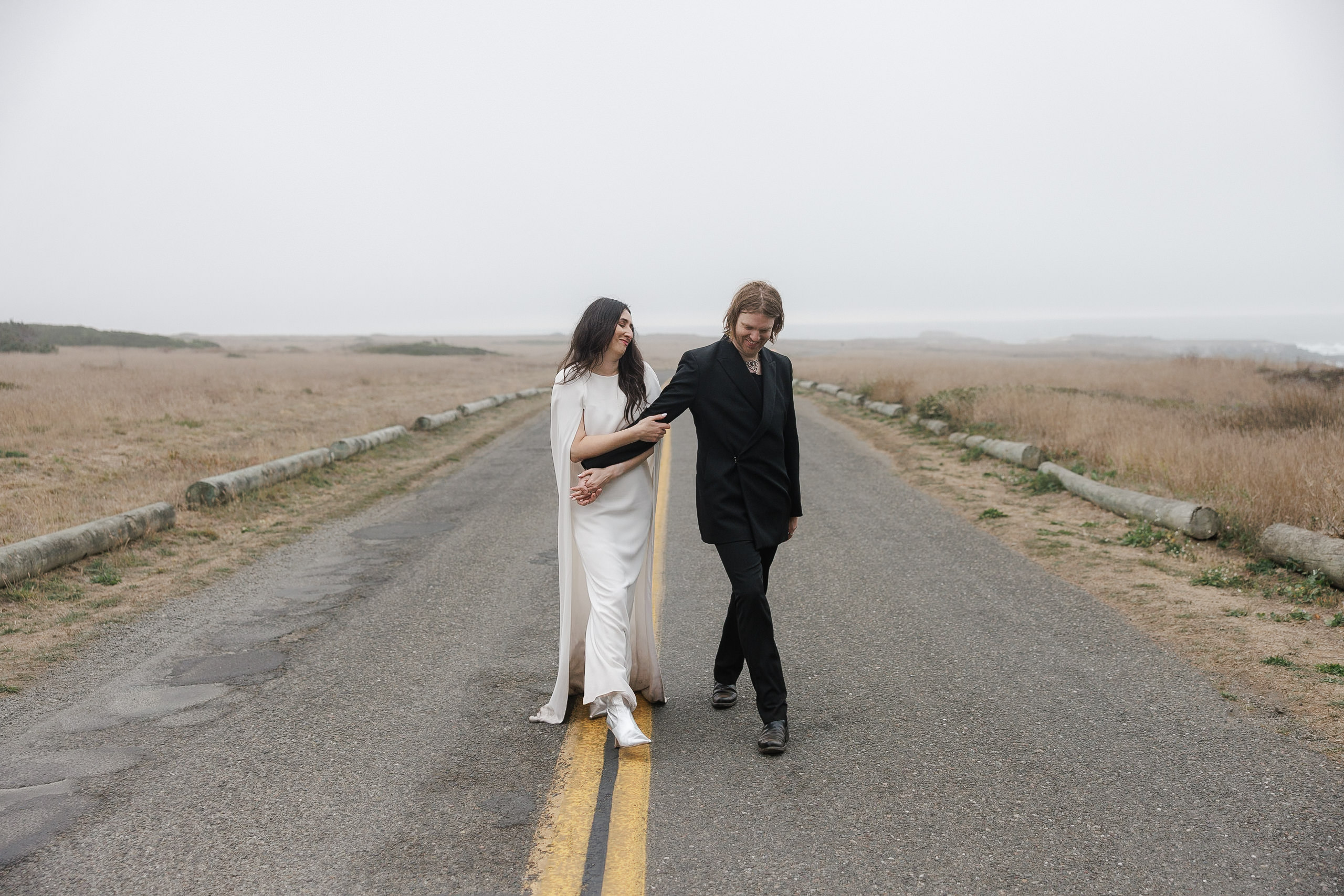 Elegant wedding photography: Couple walks hand in hand on a secluded Mendocino road.