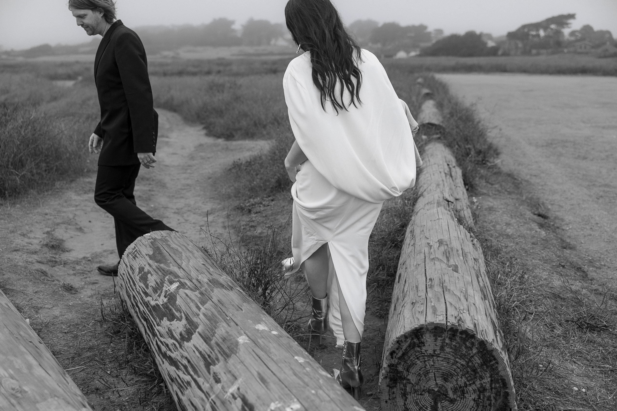Black-and-white photo of a couple in wedding attire walking in misty Mendocino landscape.