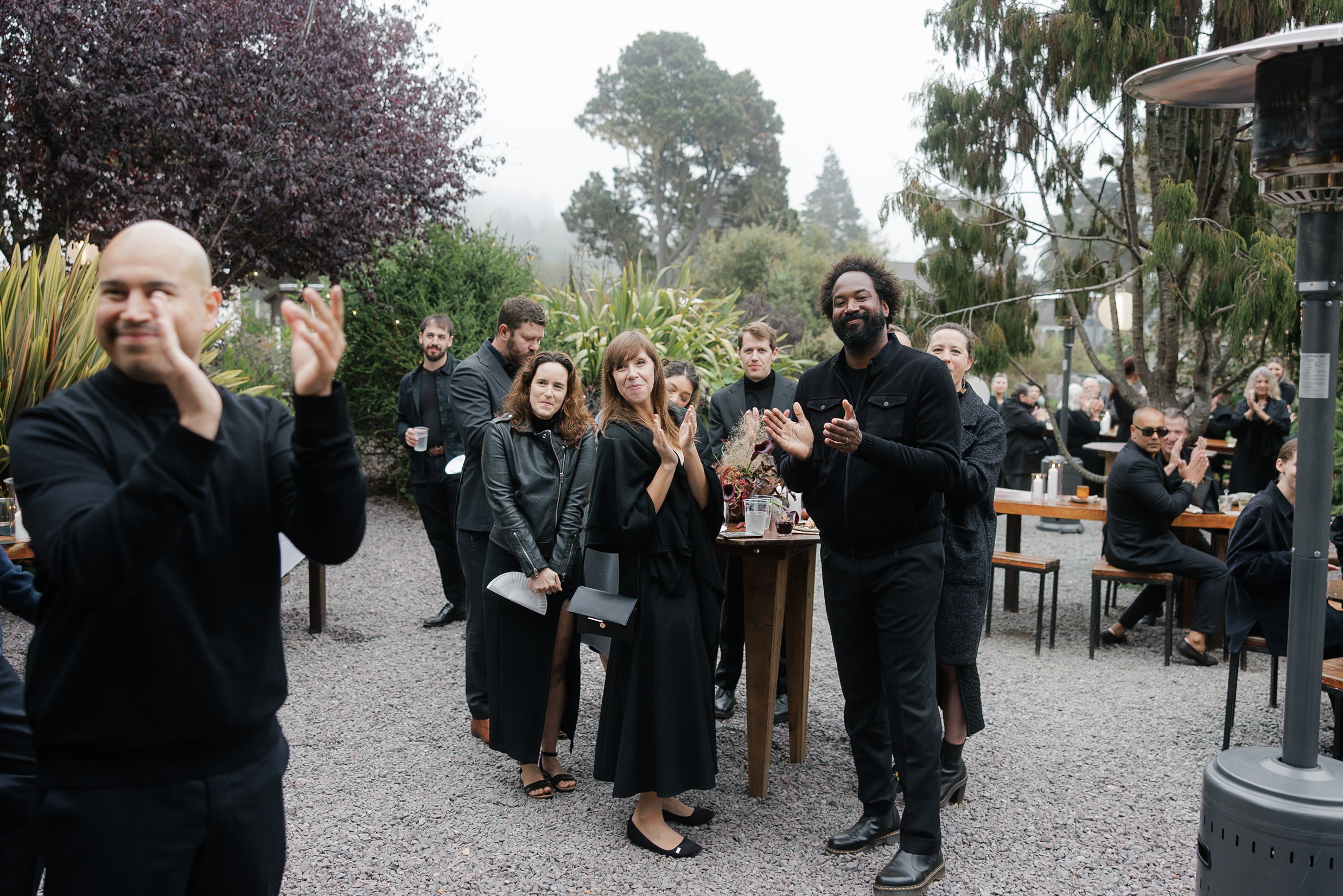 Elegant outdoor gathering in Mendocino: Celebrating amidst foggy trees and chic black attire.