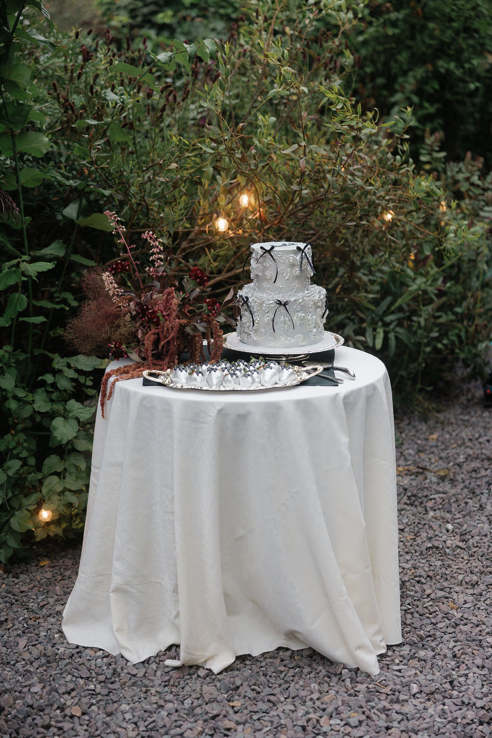 Elegant two-tiered cake with bow in Mendocinos greenery, beautifully lit, on a white-draped table.