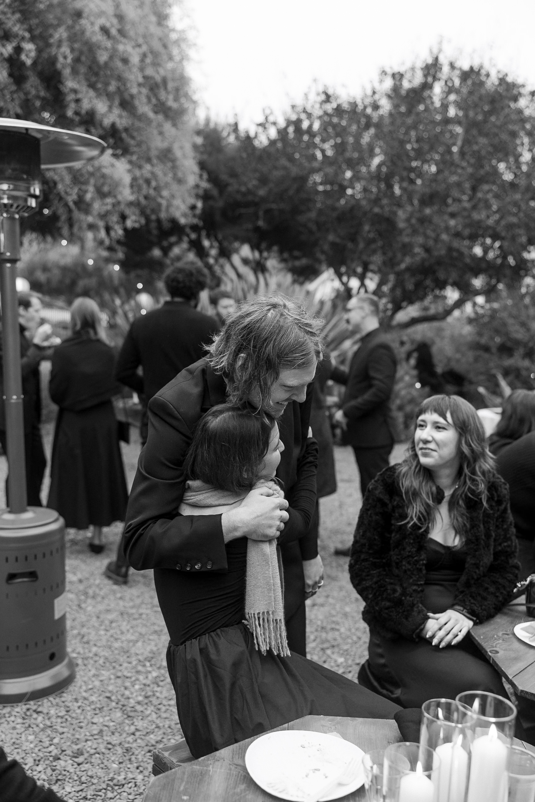 Black & white wedding moment: Couple embrace at Mendocino outdoor gathering. Elegant, candid photography.