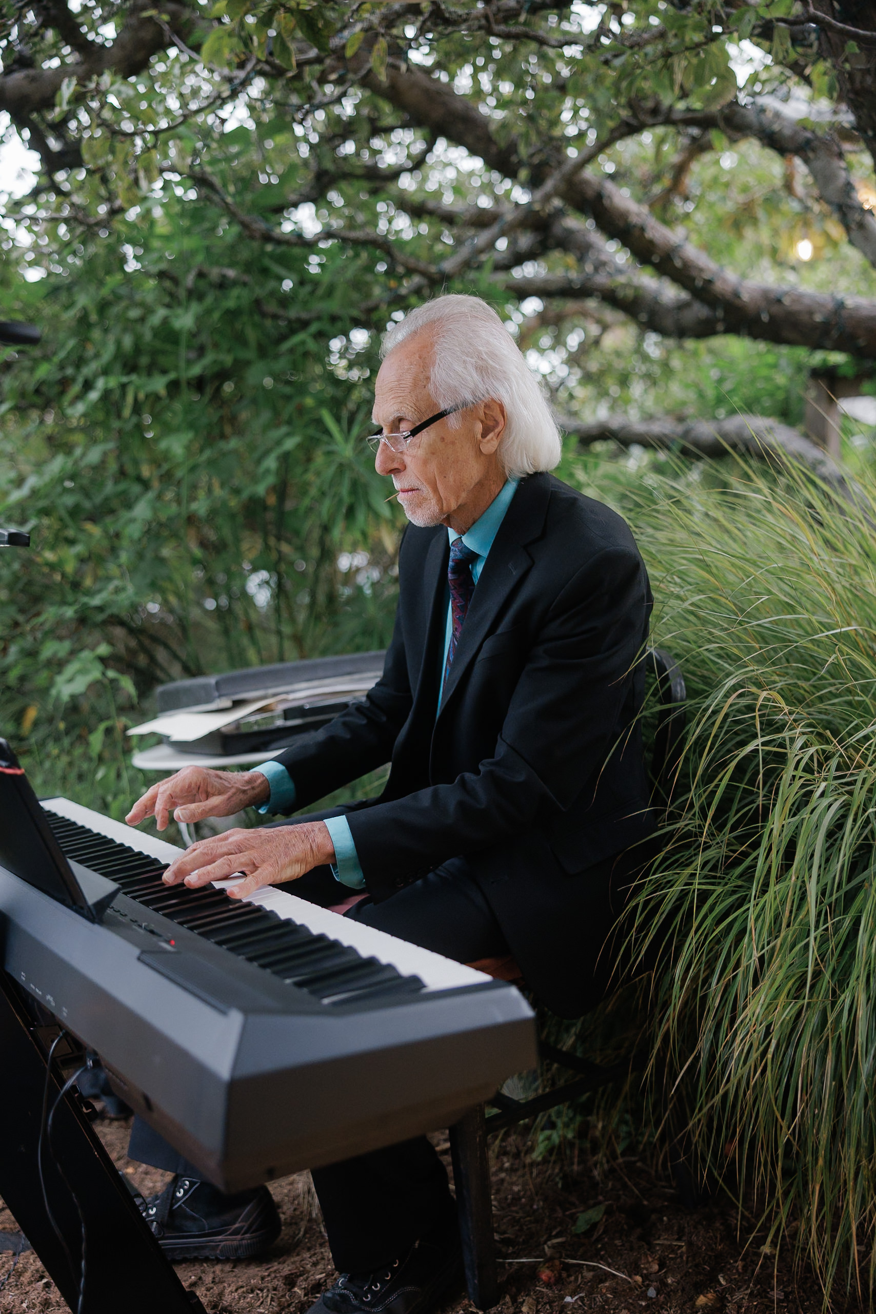 Elderly Pianist in Black Suit Surrounded by Lush Greenery in Mendocino Wedding Scene.