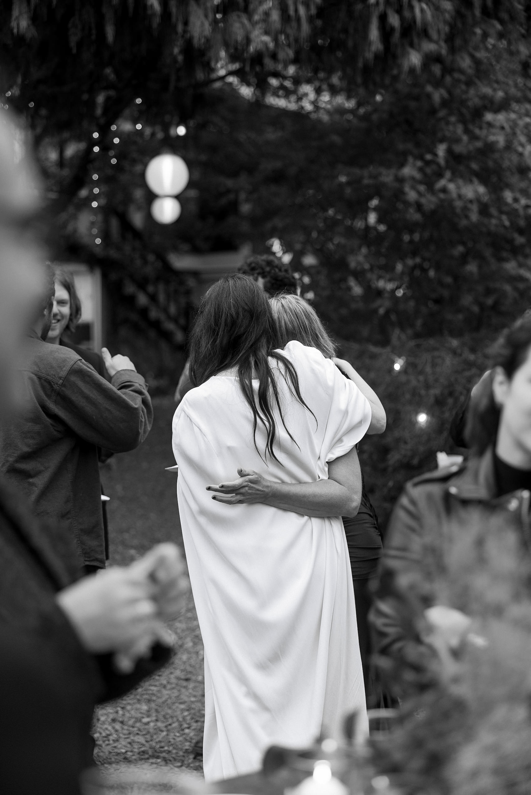 Black-and-white Mendocino wedding photo: intimate embrace, string lights in forest backdrop.