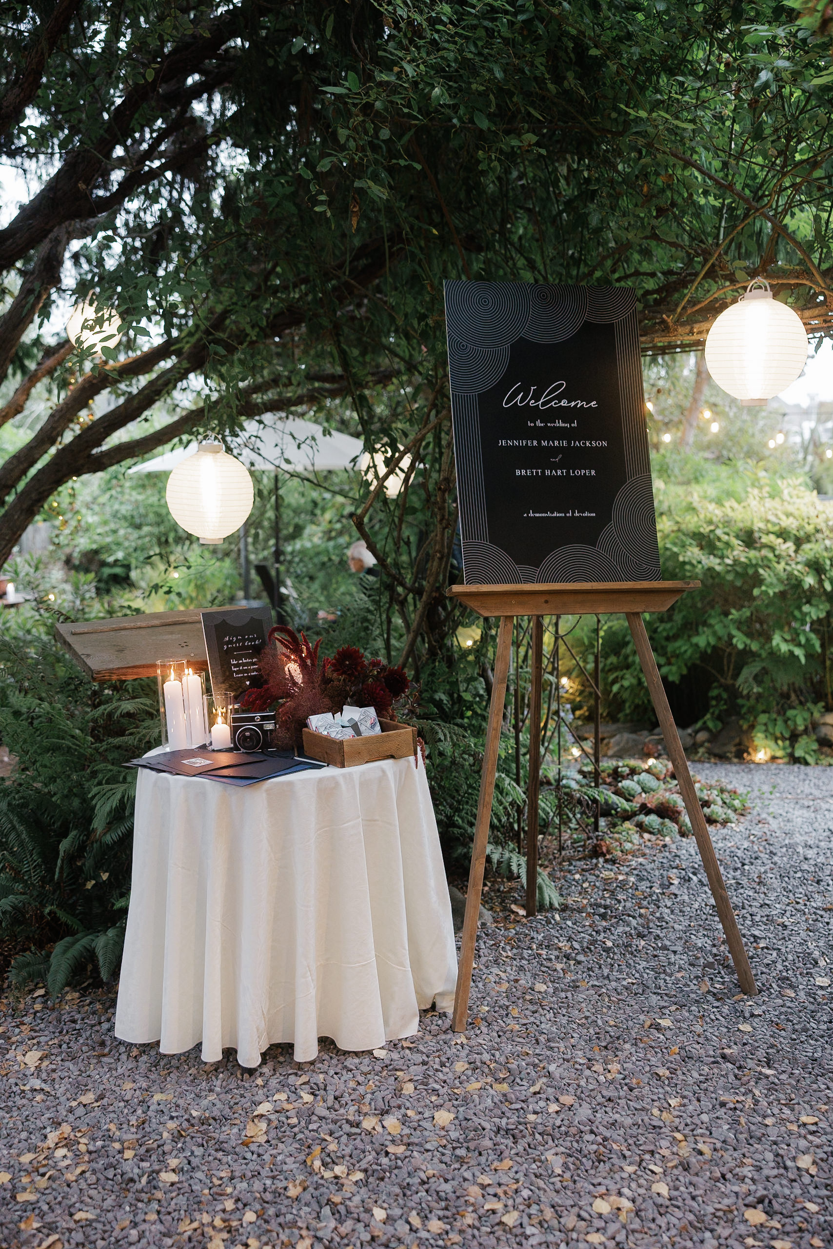 Wedding welcome sign amid lush greenery, Mendocino elegance captured. Perfect outdoor setting with candles & camera.