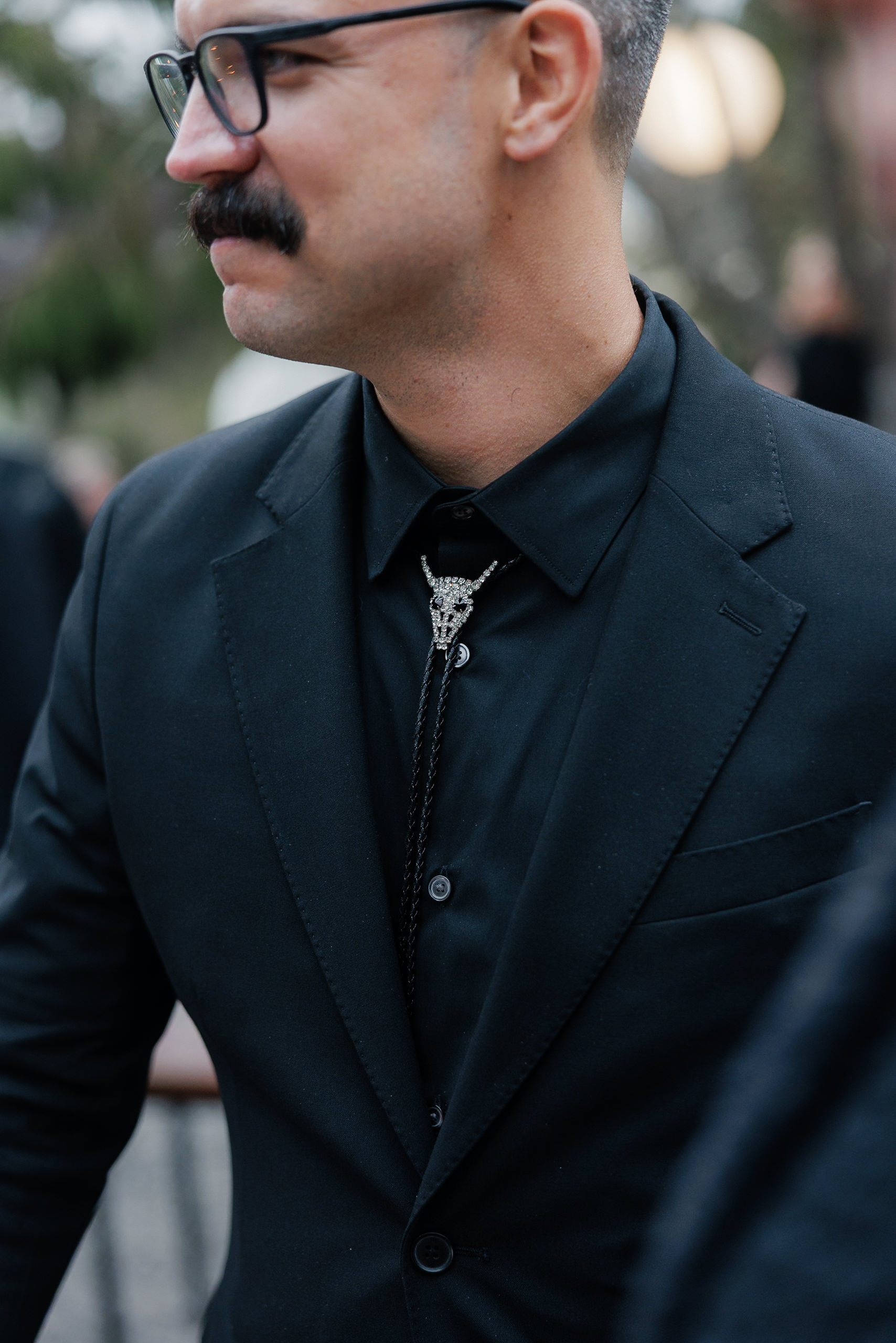 Elegant groom in black suit with skull bolo tie amidst Mendocino’s enchanting outdoor backdrop.