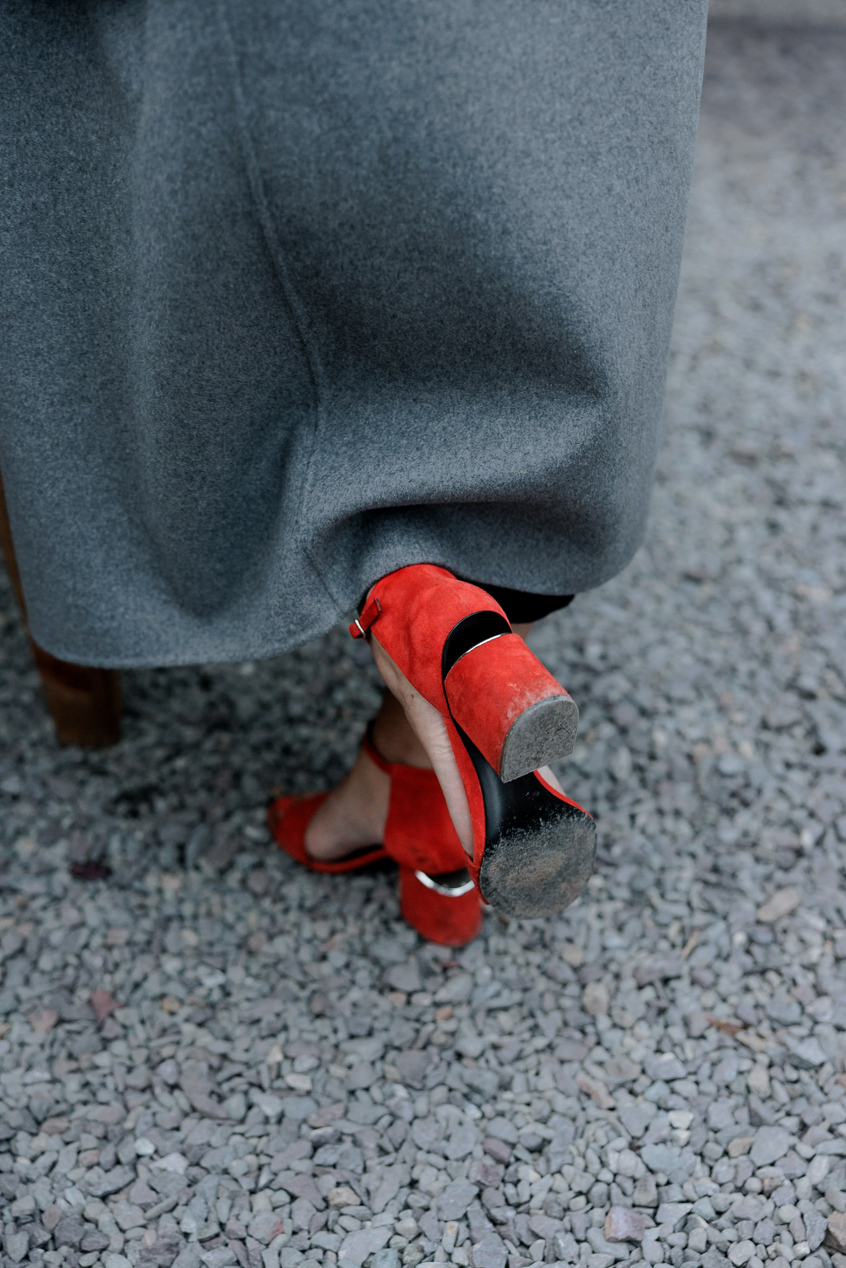 Elegant red high heels on gravel in Mendocino; perfect contrast with a gray coat. High-end wedding photography.