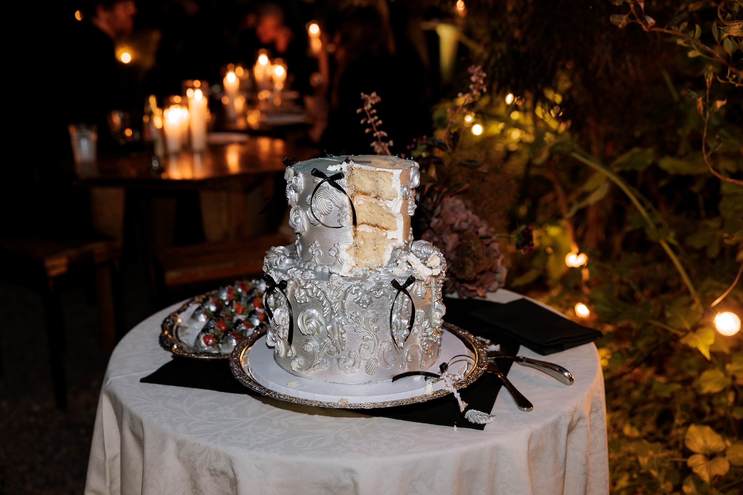 Luxurious wedding cake with silver details, black bows; candlelit Mendocino setting.