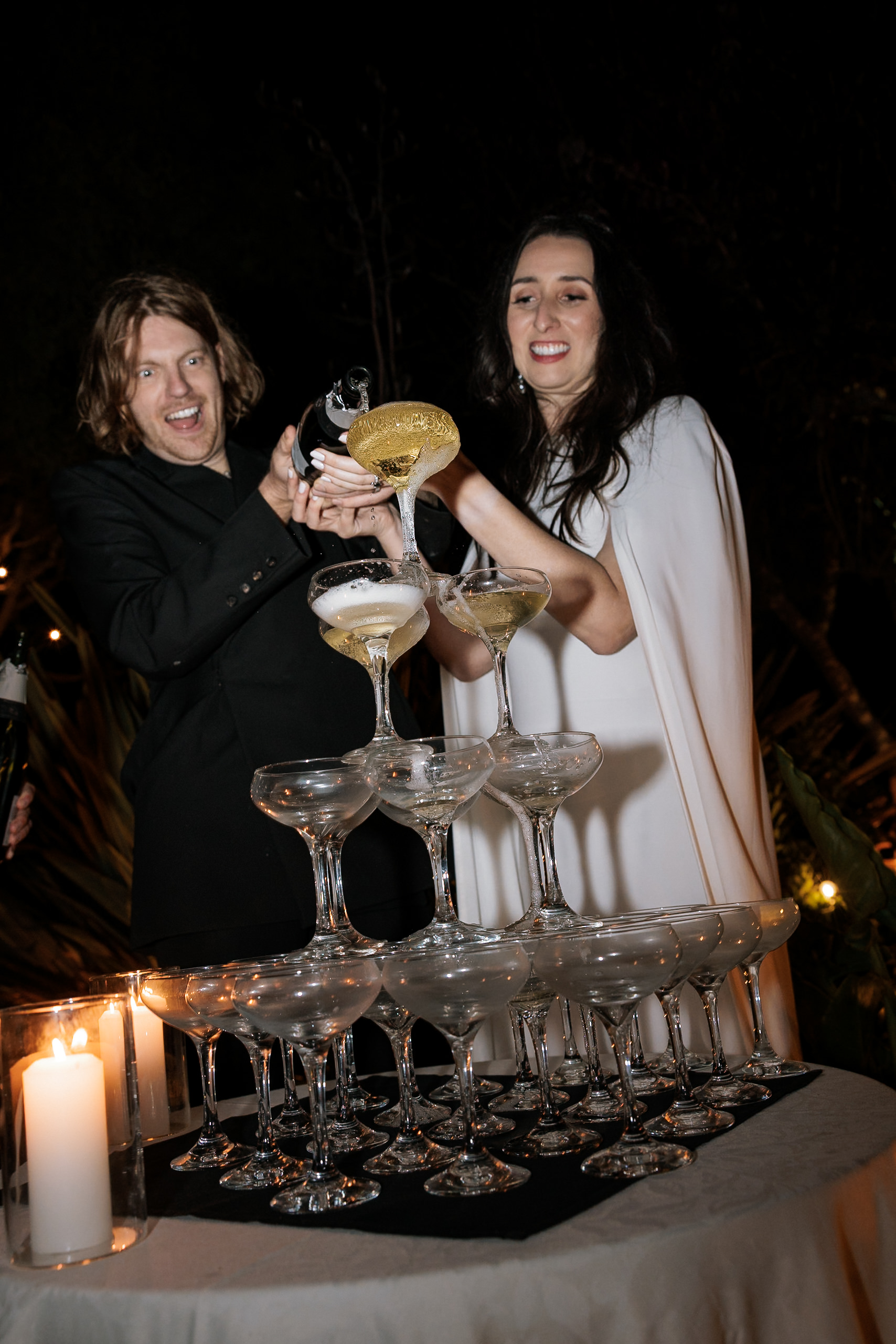 Captivating Champagne Pour: Elegant Couple in White and Black Under Candlelit Mendocino Ambiance.