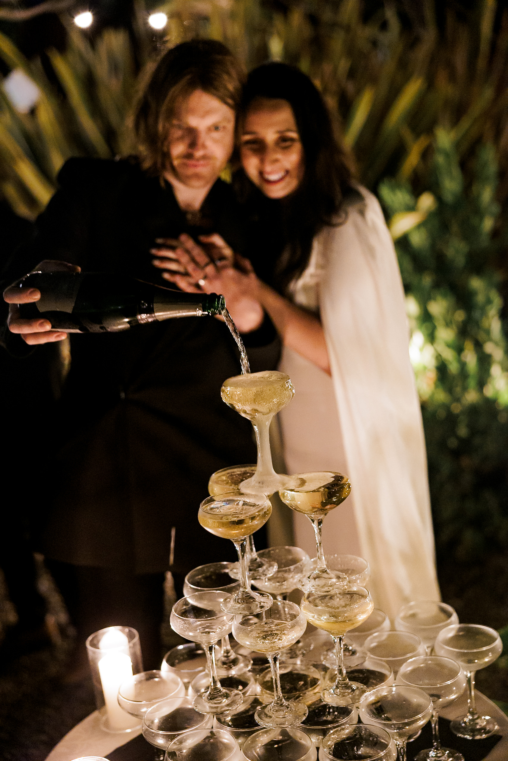 Elegant Champagne Pyramid Pouring at Outdoor Mendocino Wedding with Candlelit Ambiance.
