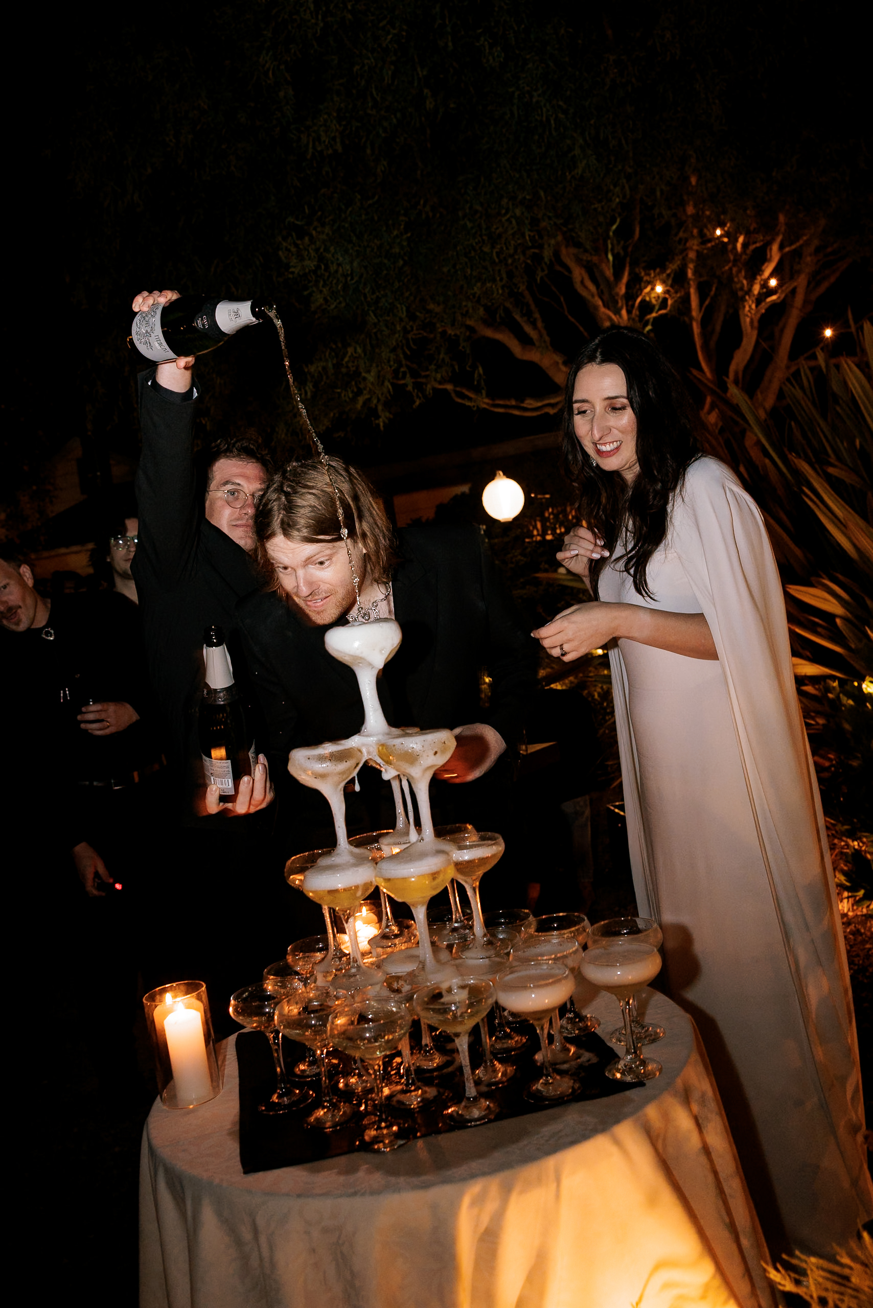 Elegant outdoor wedding in Mendocino: Champagne tower pour, festive ambiance with candles and foliage.